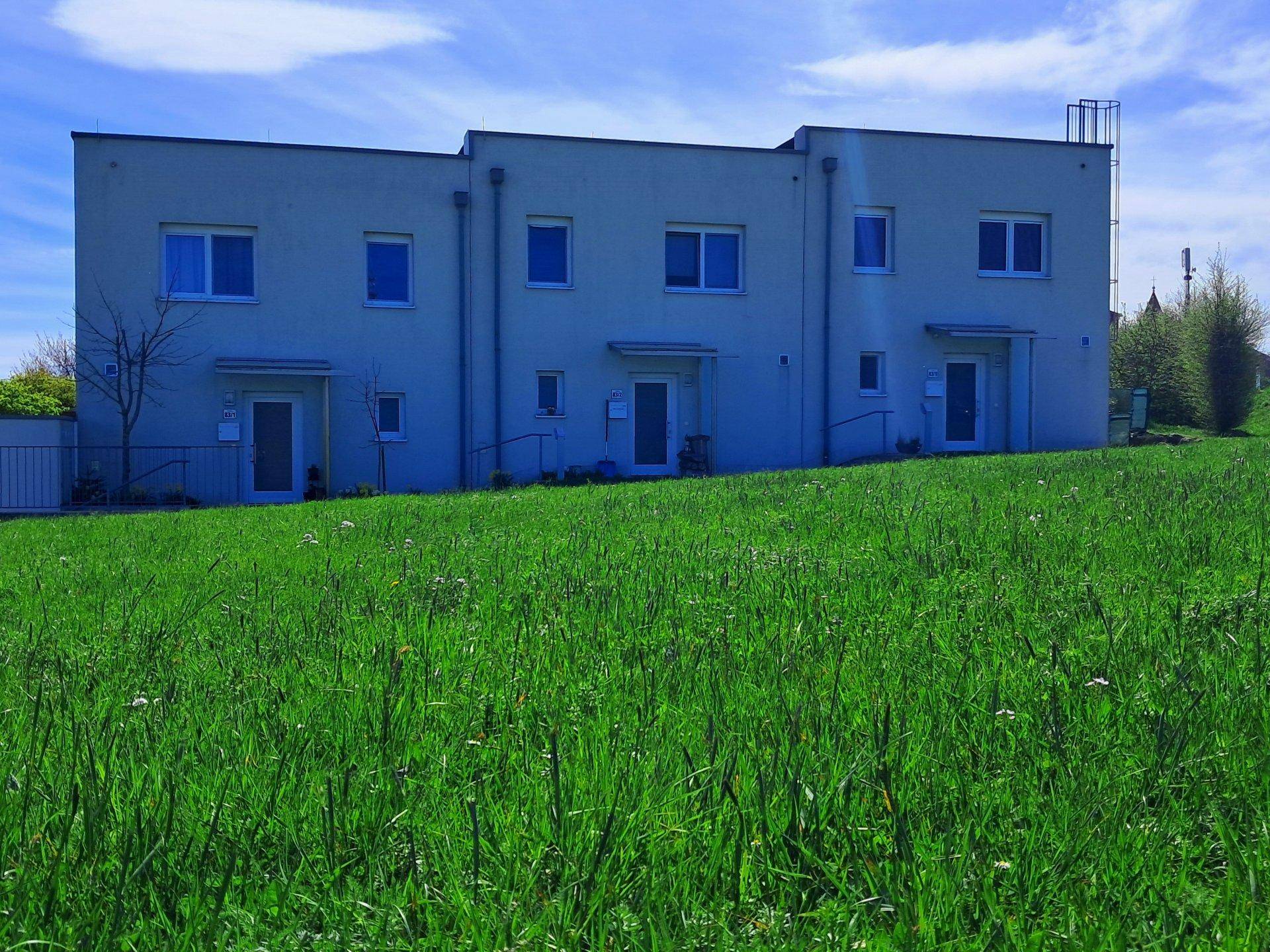 Moderne Wohngebäude, gesehen von einer blühenden grünen Wiese unter blauem Himmel.