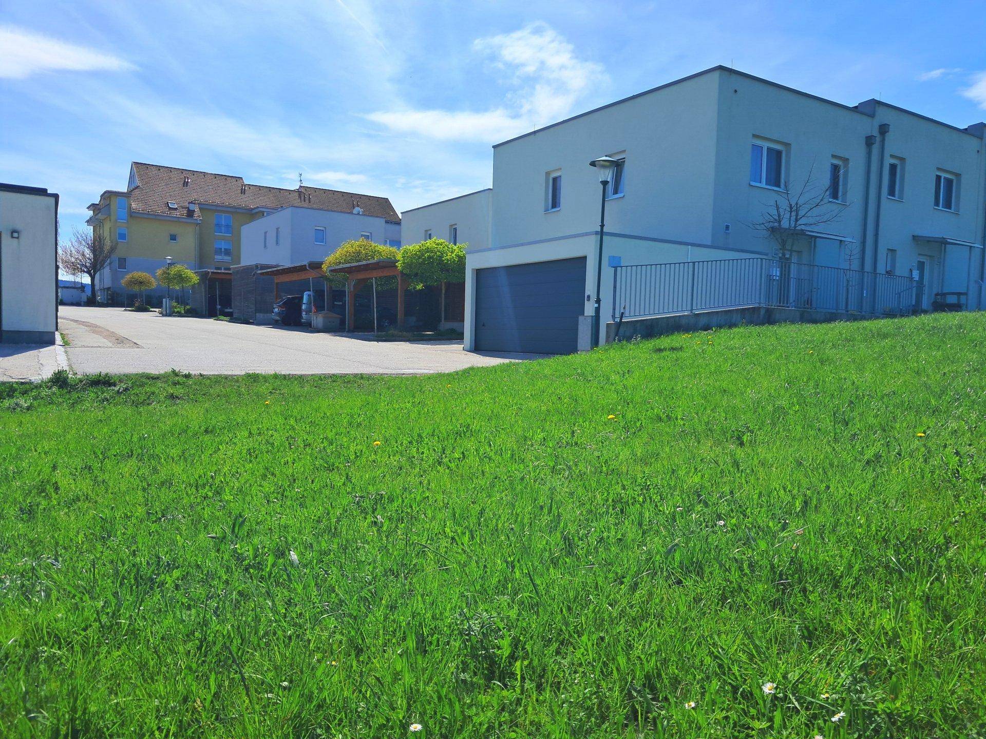 Wohngebäude mit Garage und Carports, angrenzend an eine grüne Wiese unter blauem Himmel.