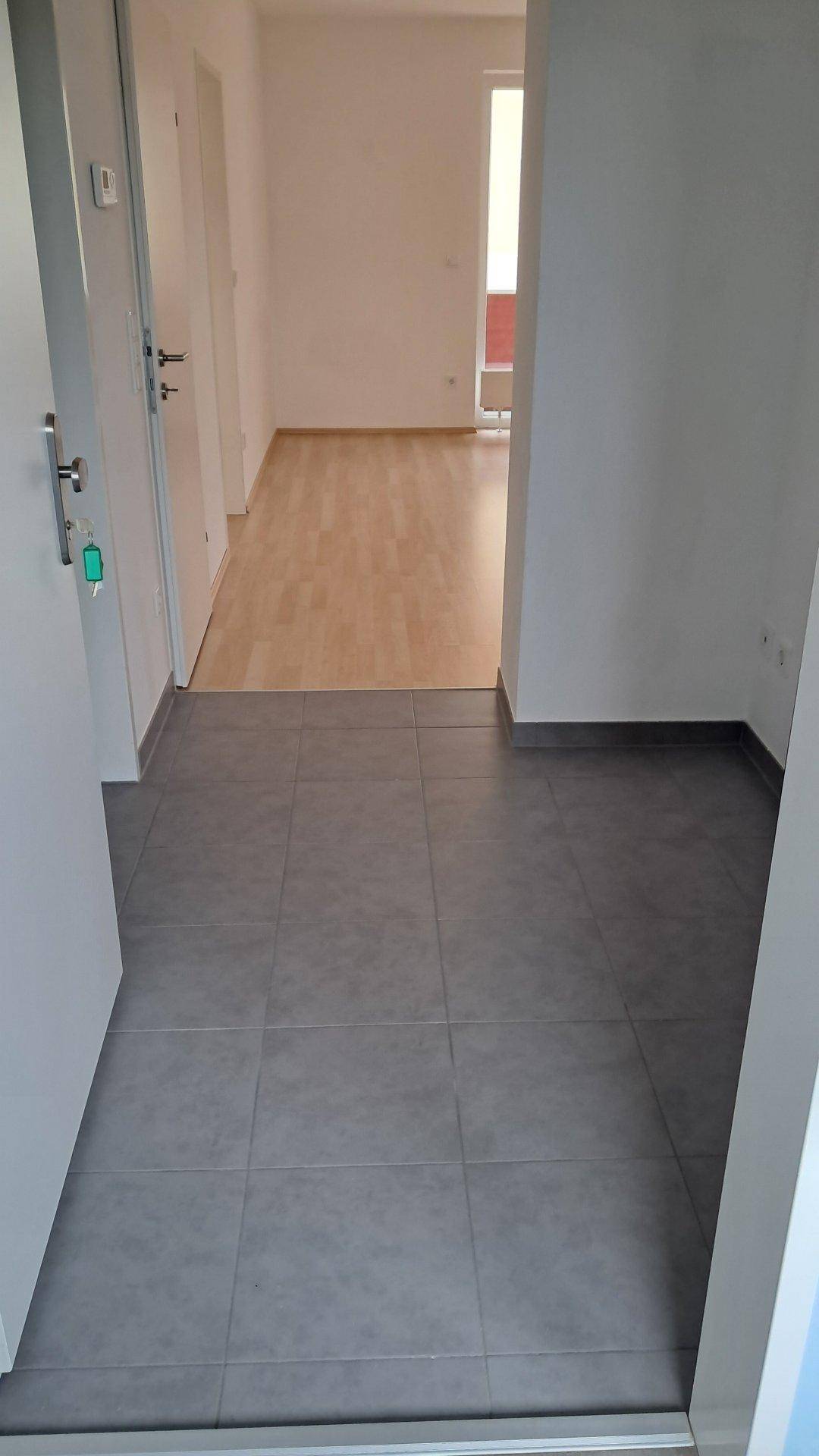 Heller Flur mit grauen Fliesen, der in einen Bereich mit hellem Laminatboden übergeht.