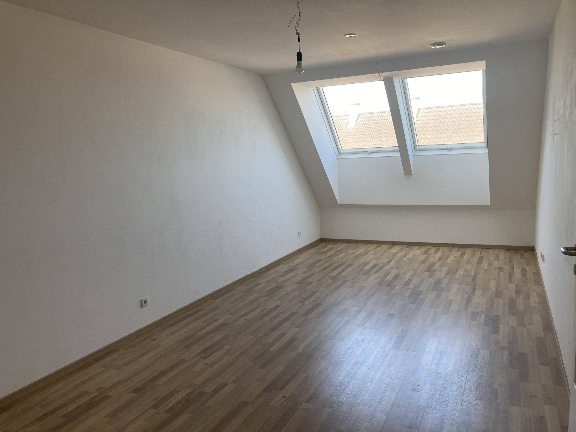 Helles Schlafzimmer im Dachgeschoss mit Holzboden, schrägen Wänden und zwei Dachfenstern.