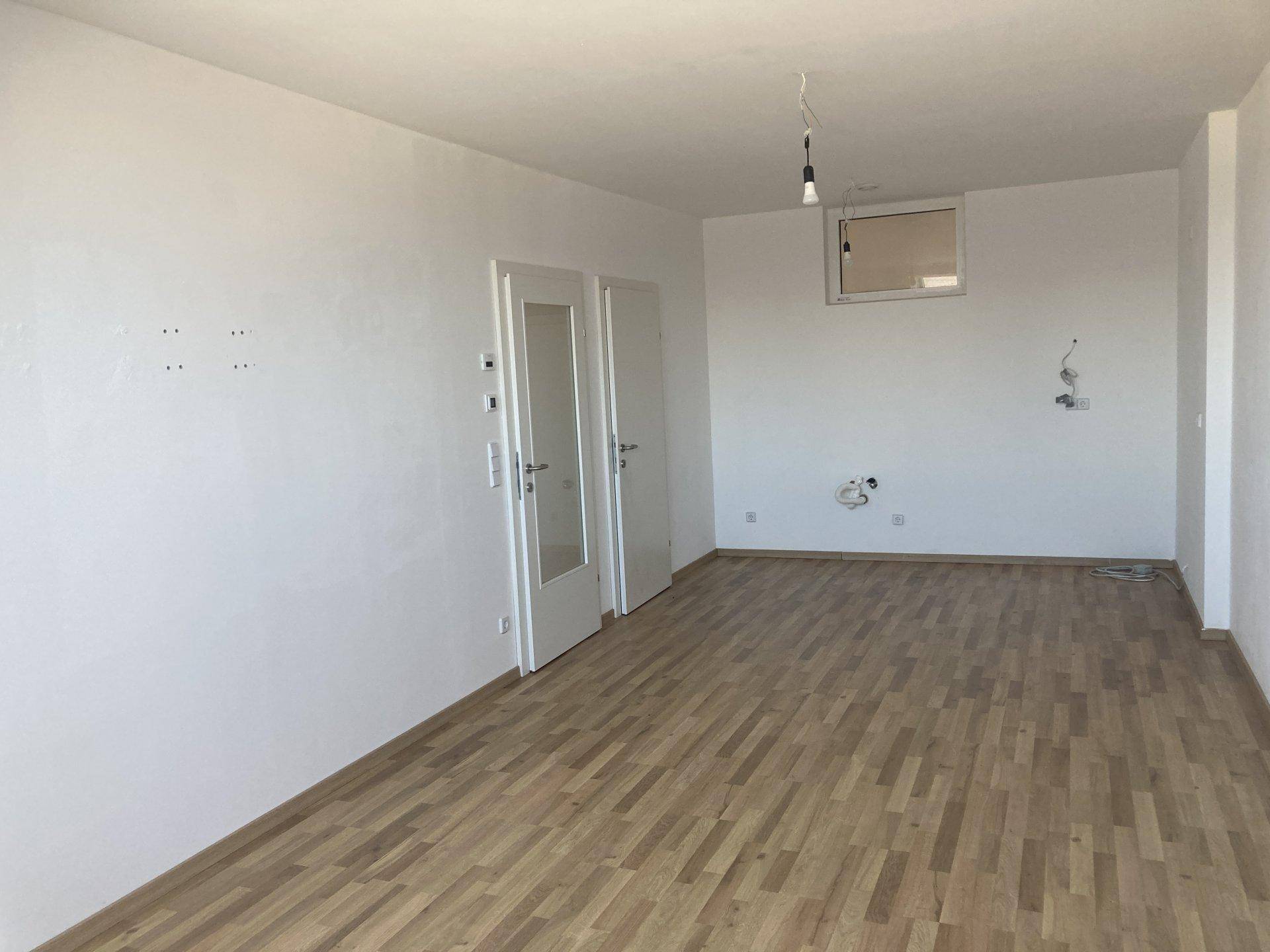 Heller, leerer Raum mit Holzboden und Anschlüssen für eine Küche, bereit zum Einbau.