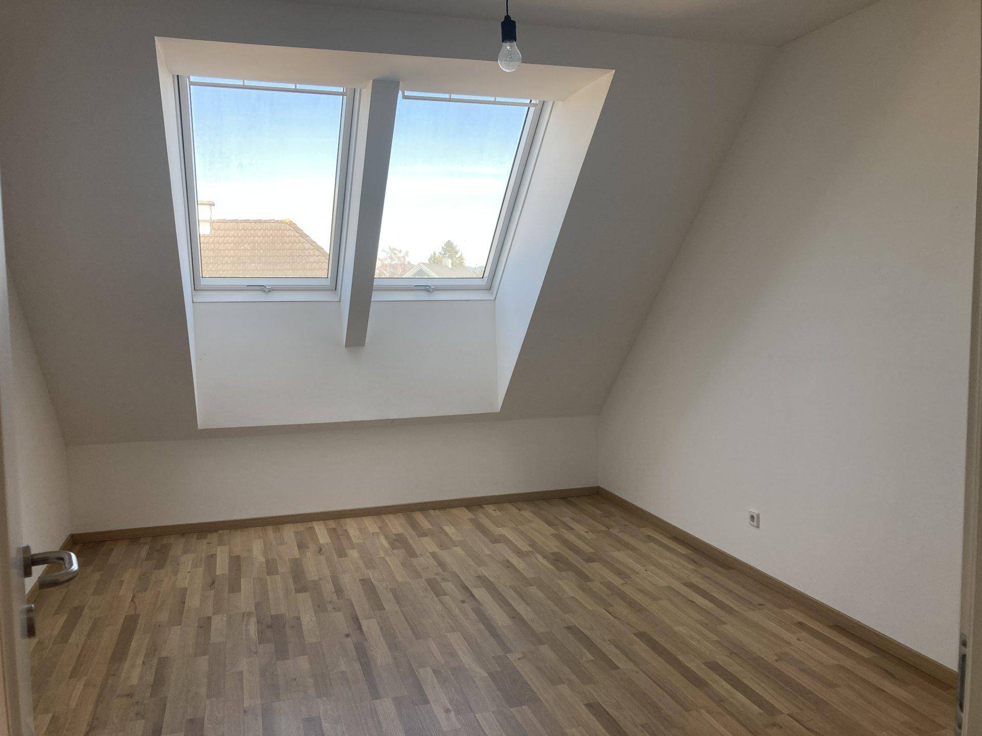 Geräumiges Schlafzimmer im Dachgeschoss mit Holzboden und zwei großen Dachfenstern für viel Licht.