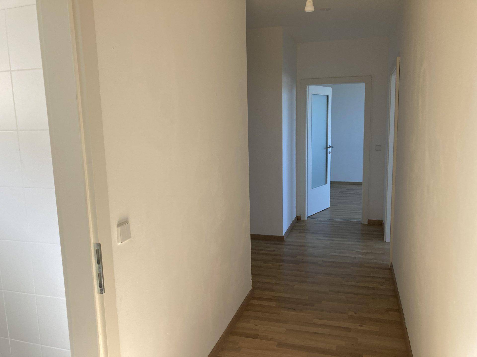 Heller Flur mit Holzboden und weißen Wänden, der zu weiteren Räumen führt.
