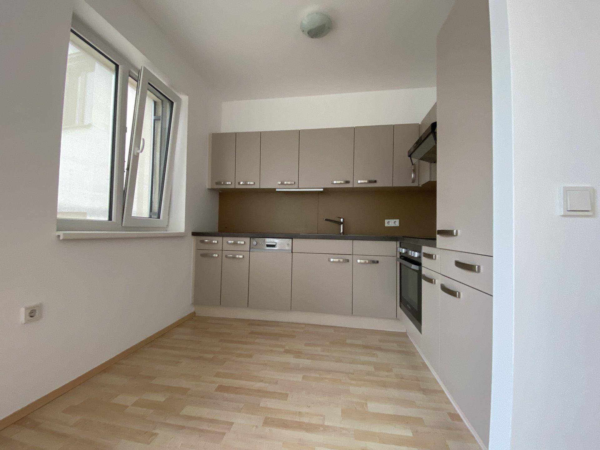Moderne Einbauküche in Beige mit integrierten Geräten und Fenster für natürliches Licht.
