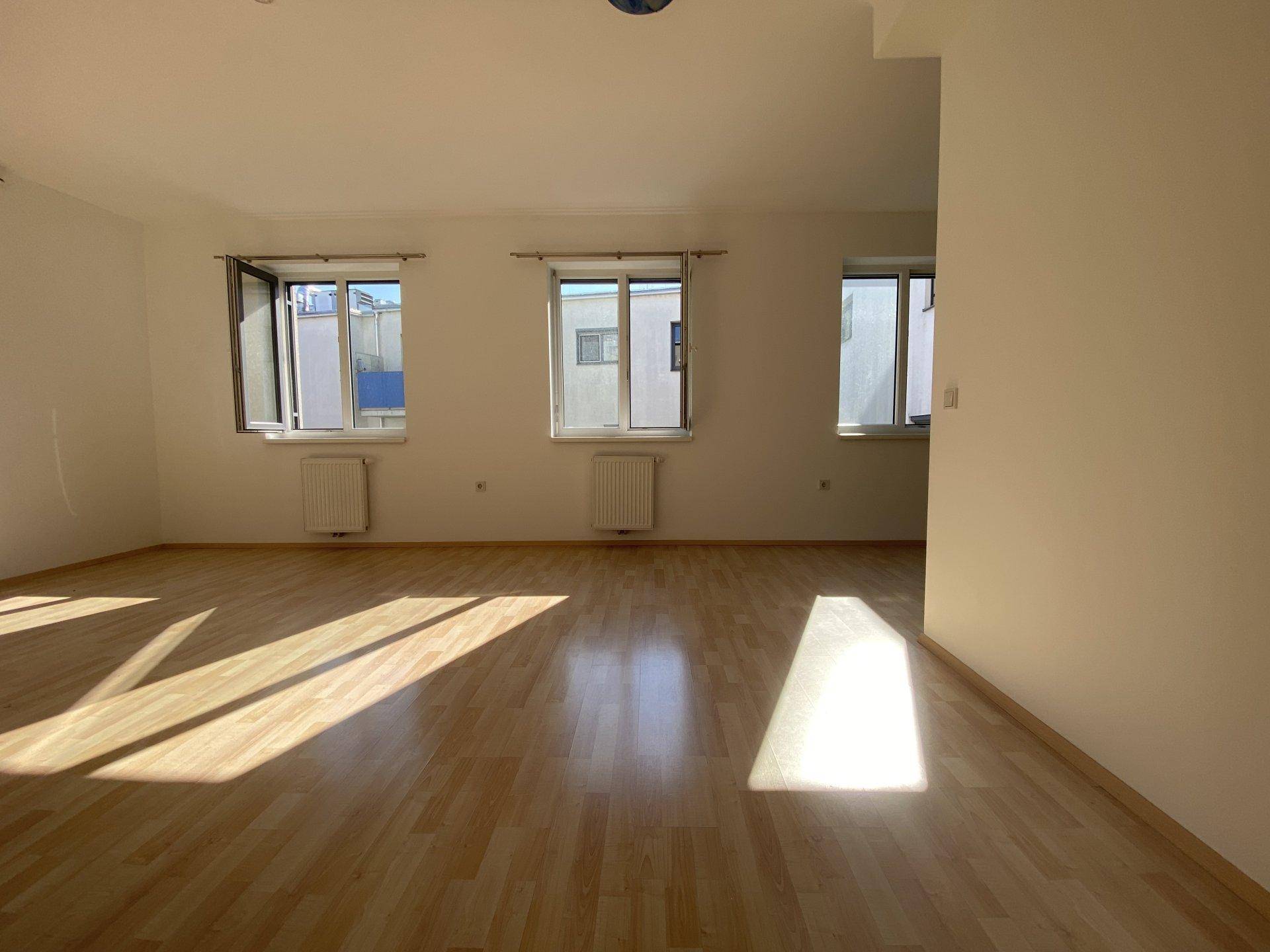 Helles Wohnzimmer mit Laminatboden und mehreren Fenstern, die den Raum gut belichten.