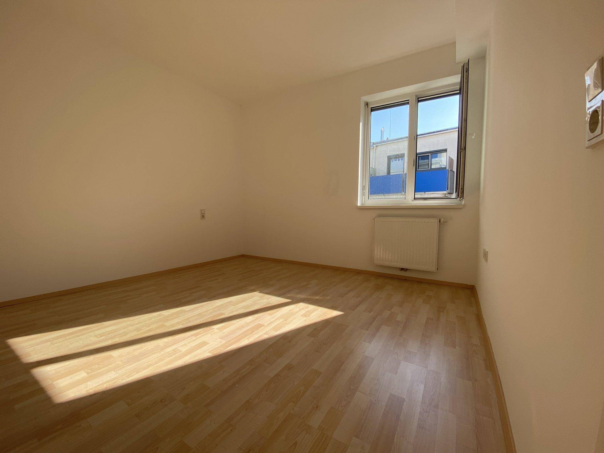 Helles Schlafzimmer mit Laminatboden und einem Fenster, das viel Tageslicht spendet.