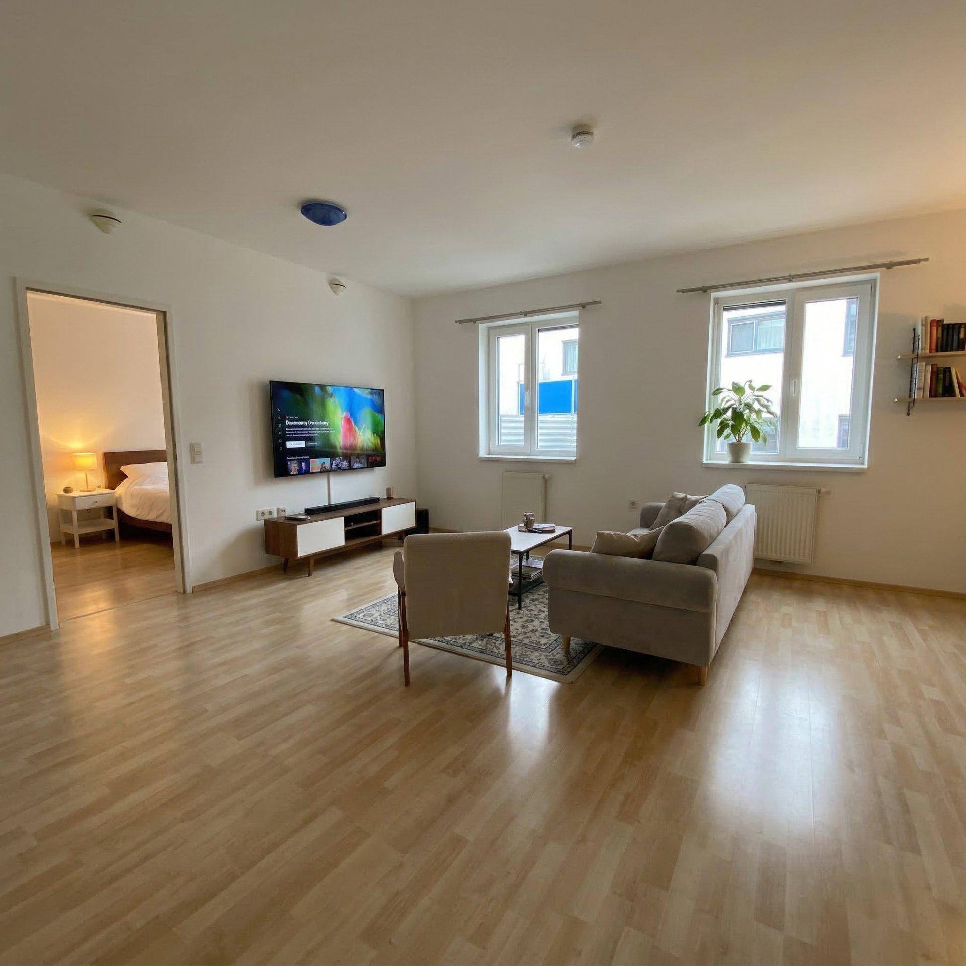 Gemütliches Wohnzimmer mit Sofa, Fernseher und Blick auf ein angrenzendes Schlafzimmer.