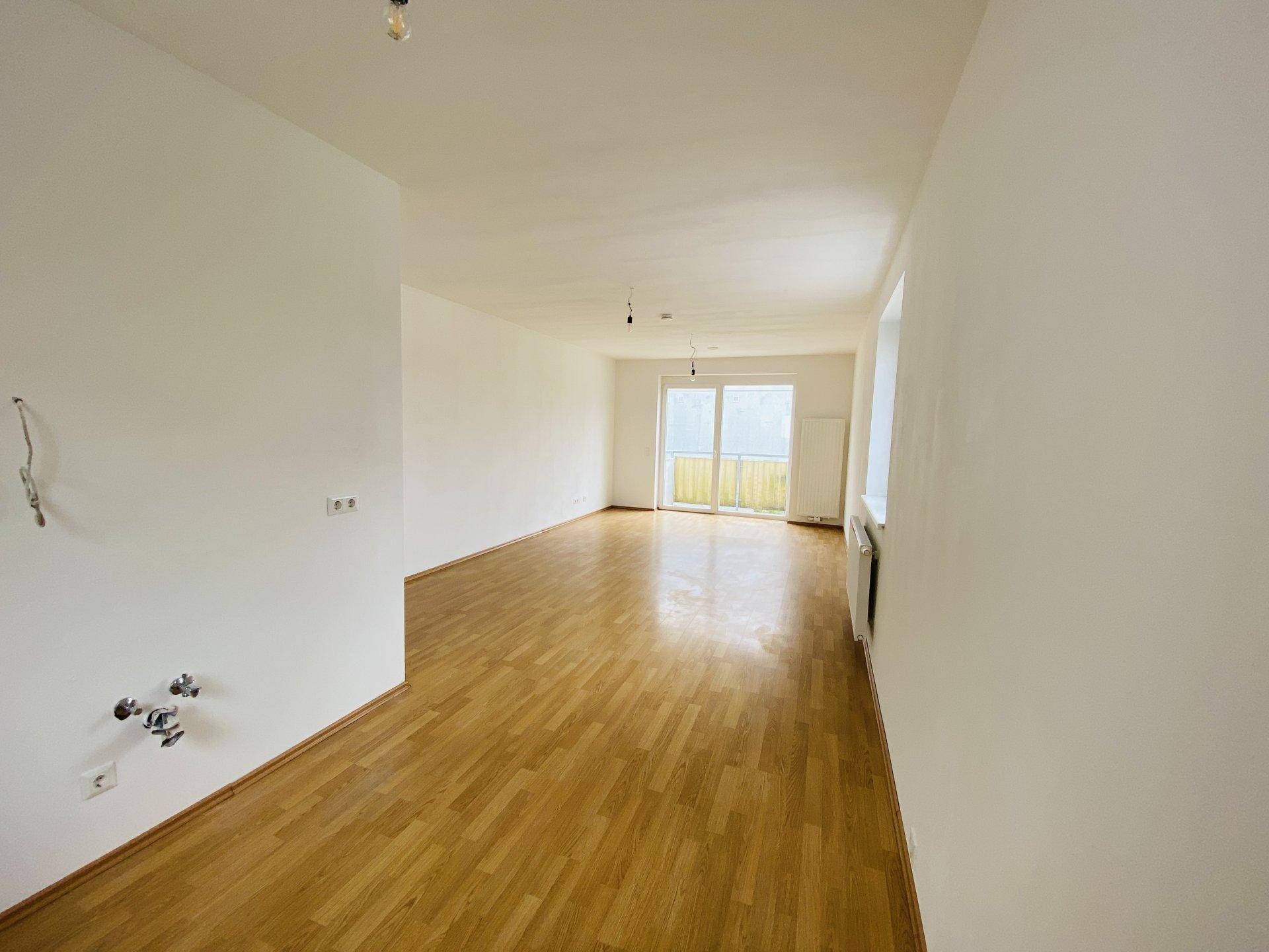 Geräumiges, helles Wohnzimmer mit Parkettboden und Zugang zu einem Balkon.