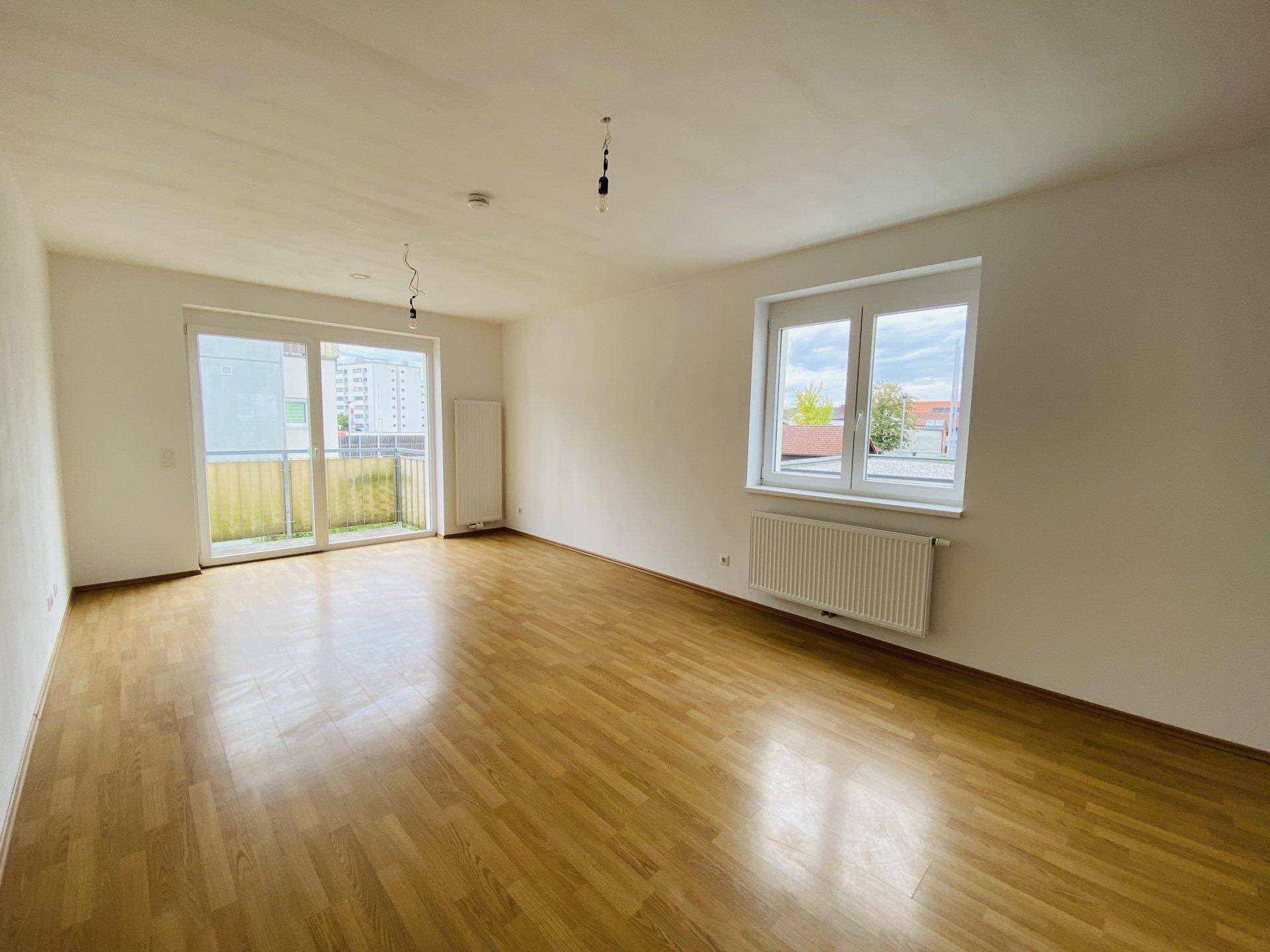 Helles Wohnzimmer mit Parkettboden, großem Fenster und Zugang zum Balkon.
