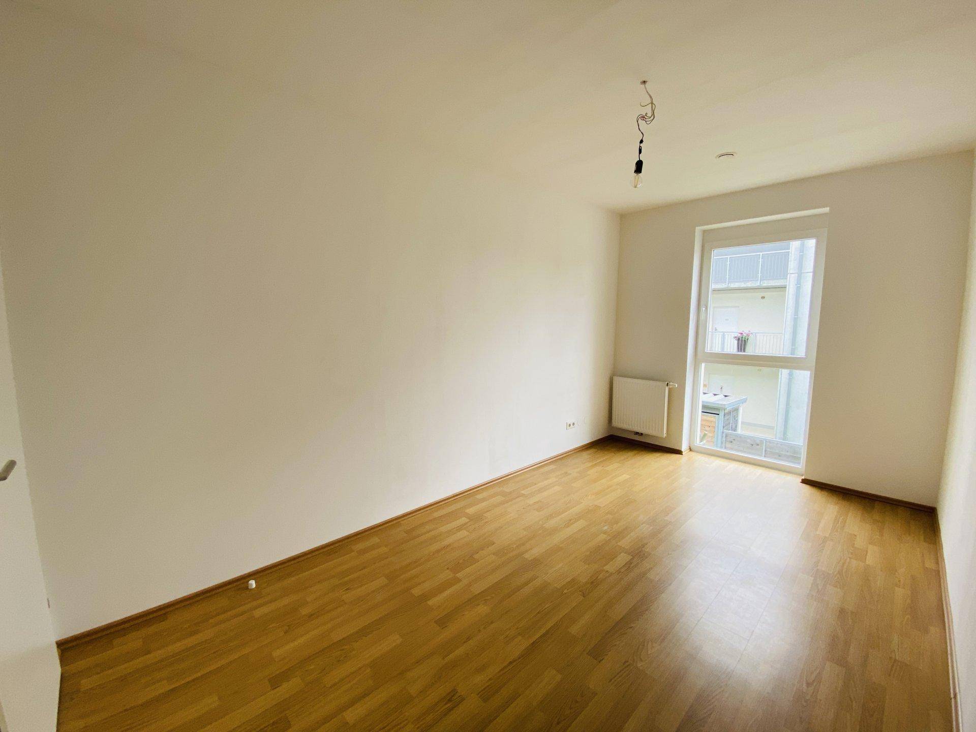 Helles Zimmer mit Parkettboden und einem Fenster mit Blick auf den Innenhof.