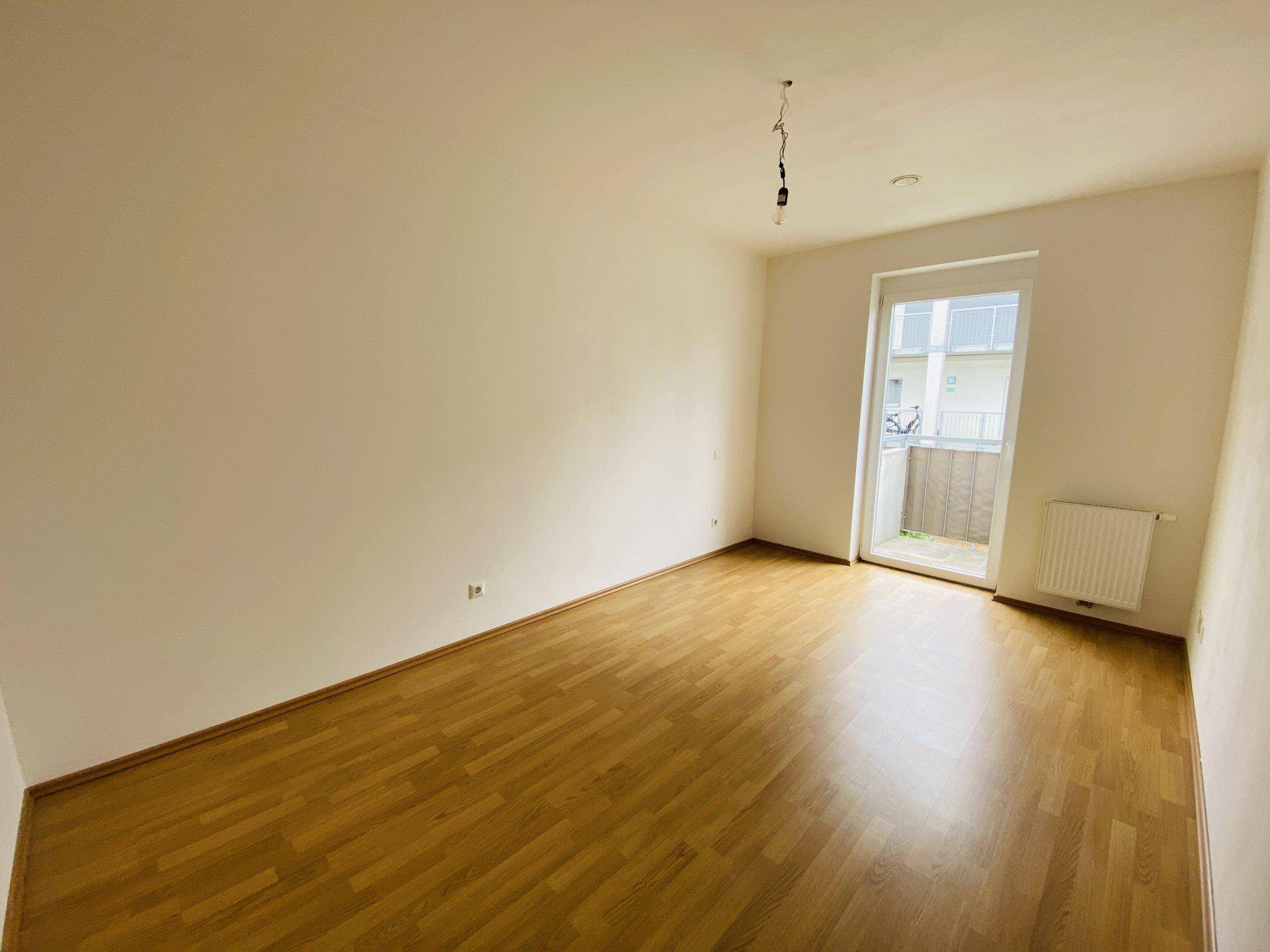 Helles Zimmer mit Parkettboden und Zugang zu einem kleinen Balkon.