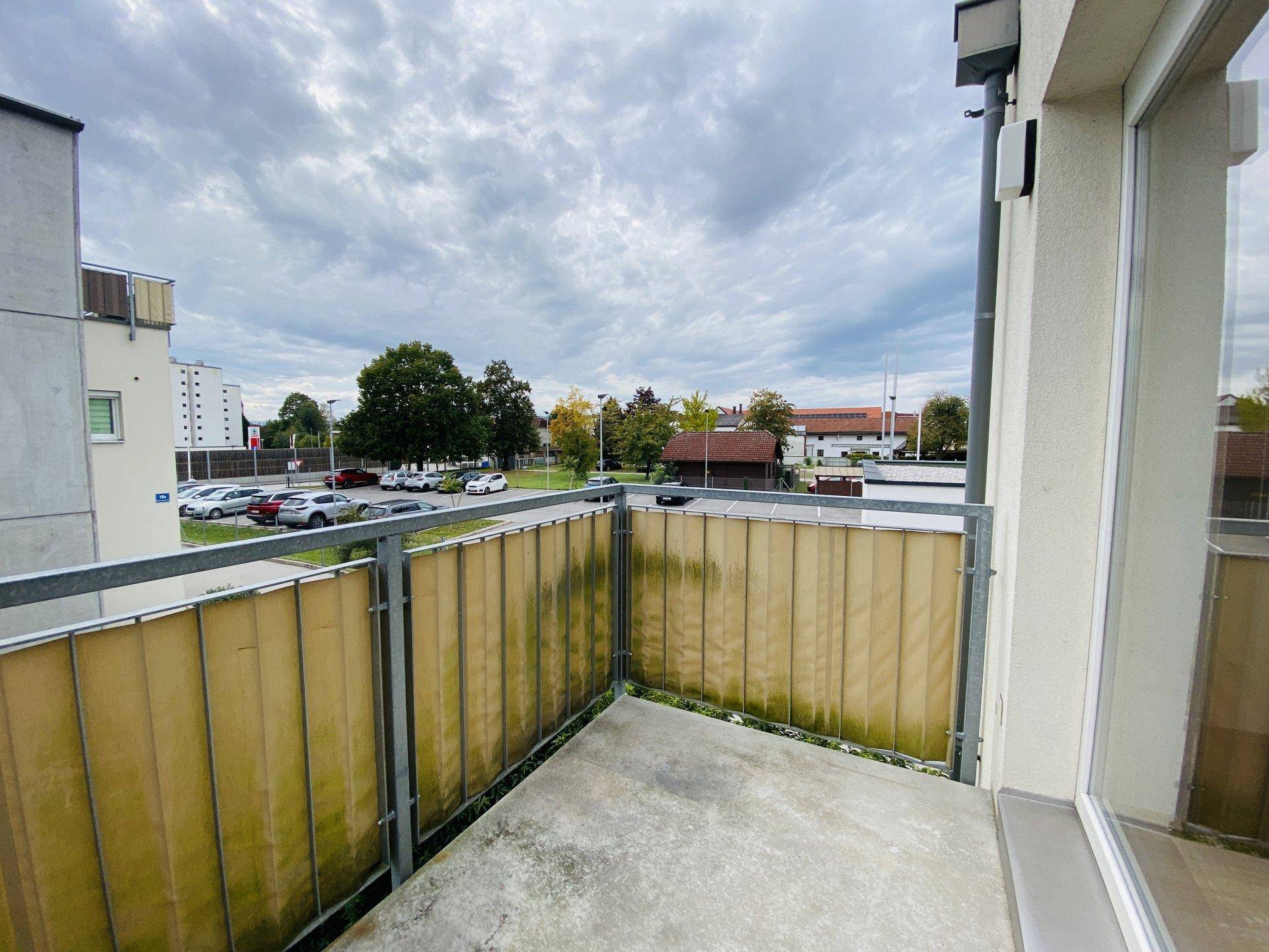 Balkon mit Blick auf einen Parkplatz und umliegende Gebäude unter bewölktem Himmel.