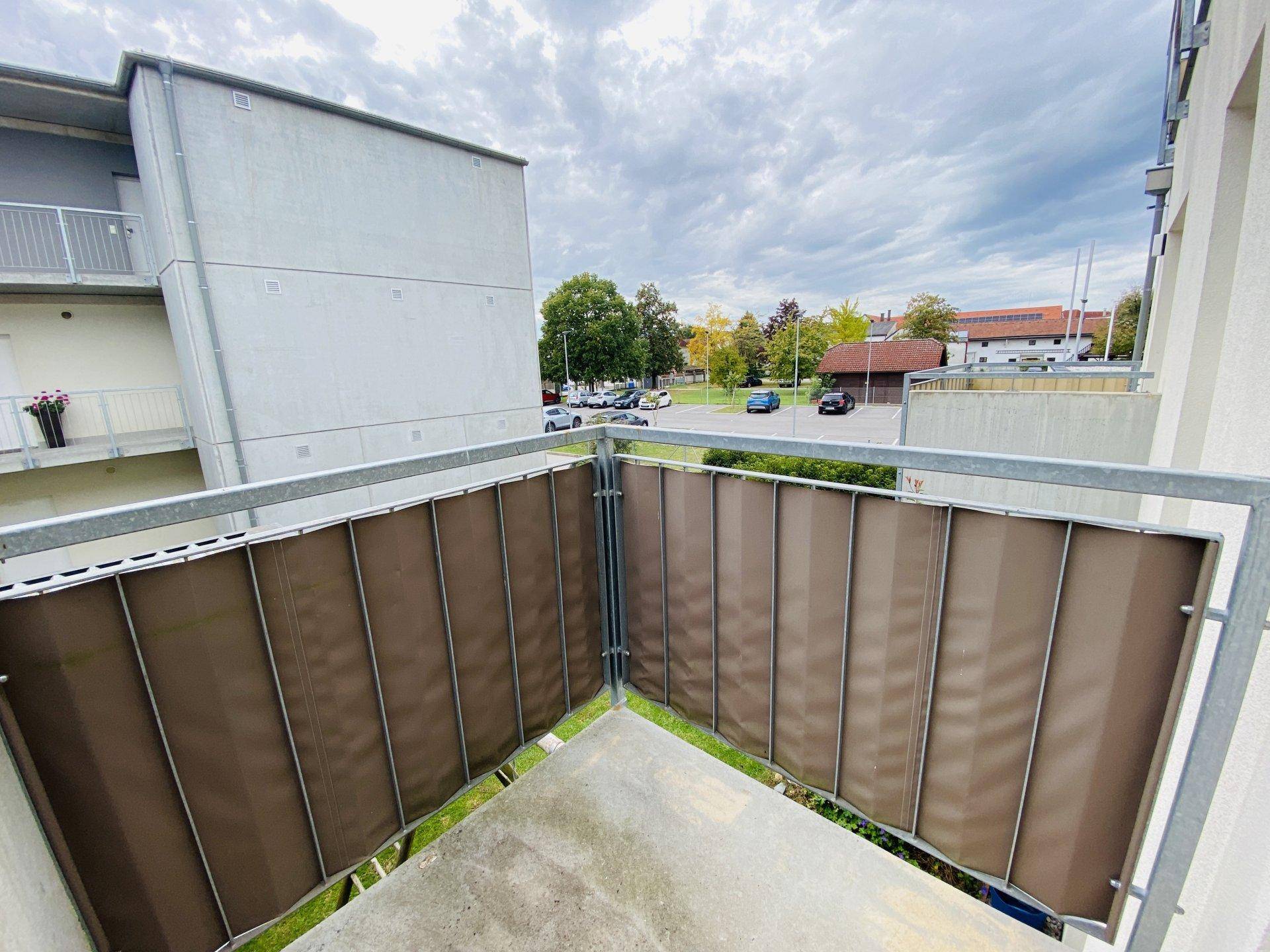 Kleiner Balkon mit Sichtschutz und Blick auf den Außenbereich und Parkplätze.