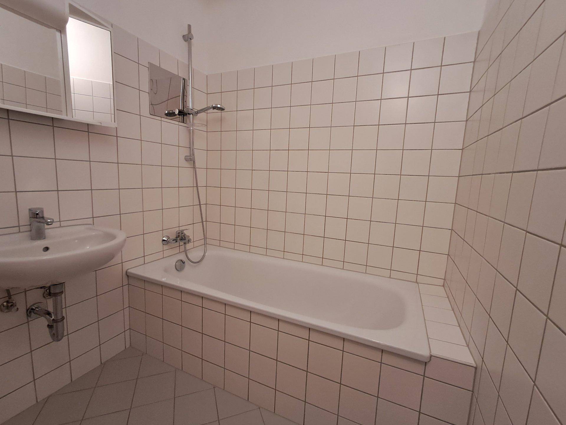 Gefliestes Badezimmer mit Badewanne, Duscharmatur und einem einzelnen Waschbecken.