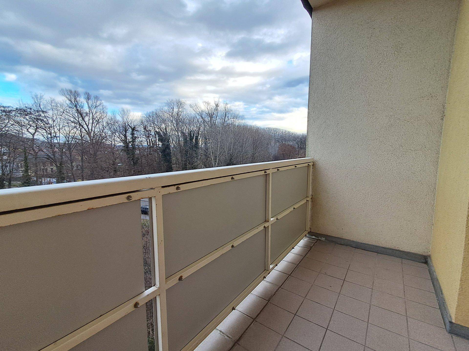 Balkon mit Fliesenboden und Blick auf Bäume und die Umgebung unter bewölktem Himmel.