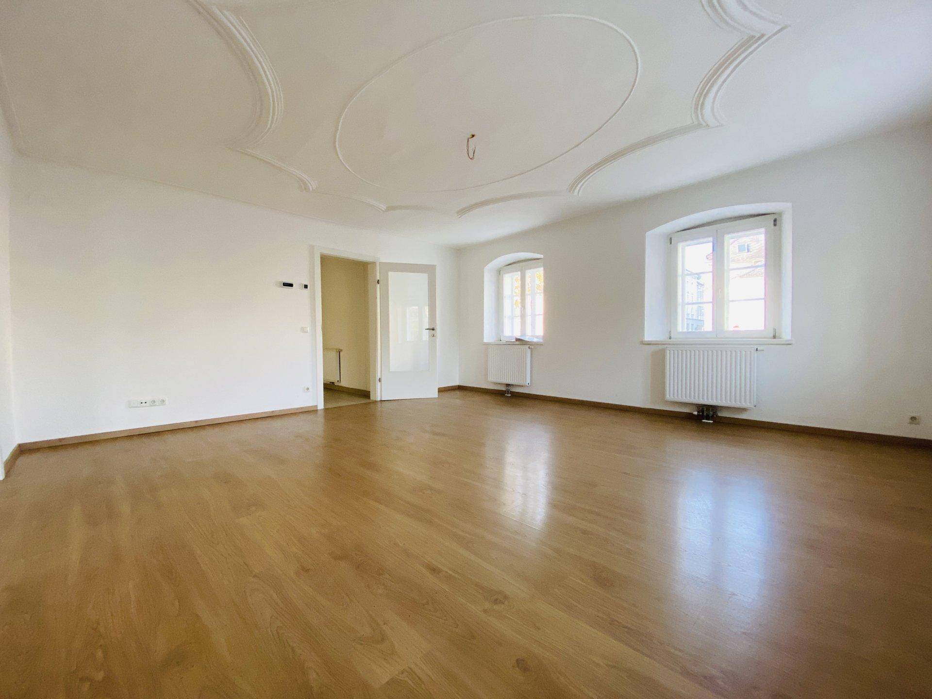 Geräumiger Raum mit Holzboden, hohen Decken und dekorativer Stuckverzierung, ideal für Wohnzwecke.