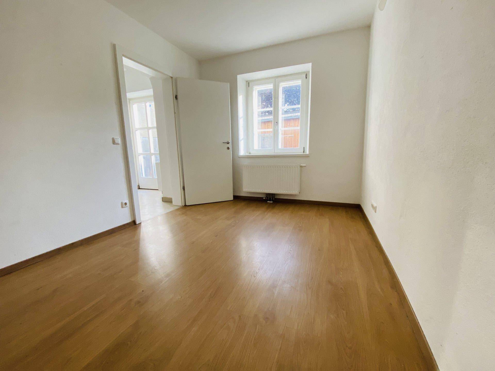 Gemütliches Schlafzimmer mit hellem Holzboden und einem Fenster, das viel Tageslicht hereinlässt.