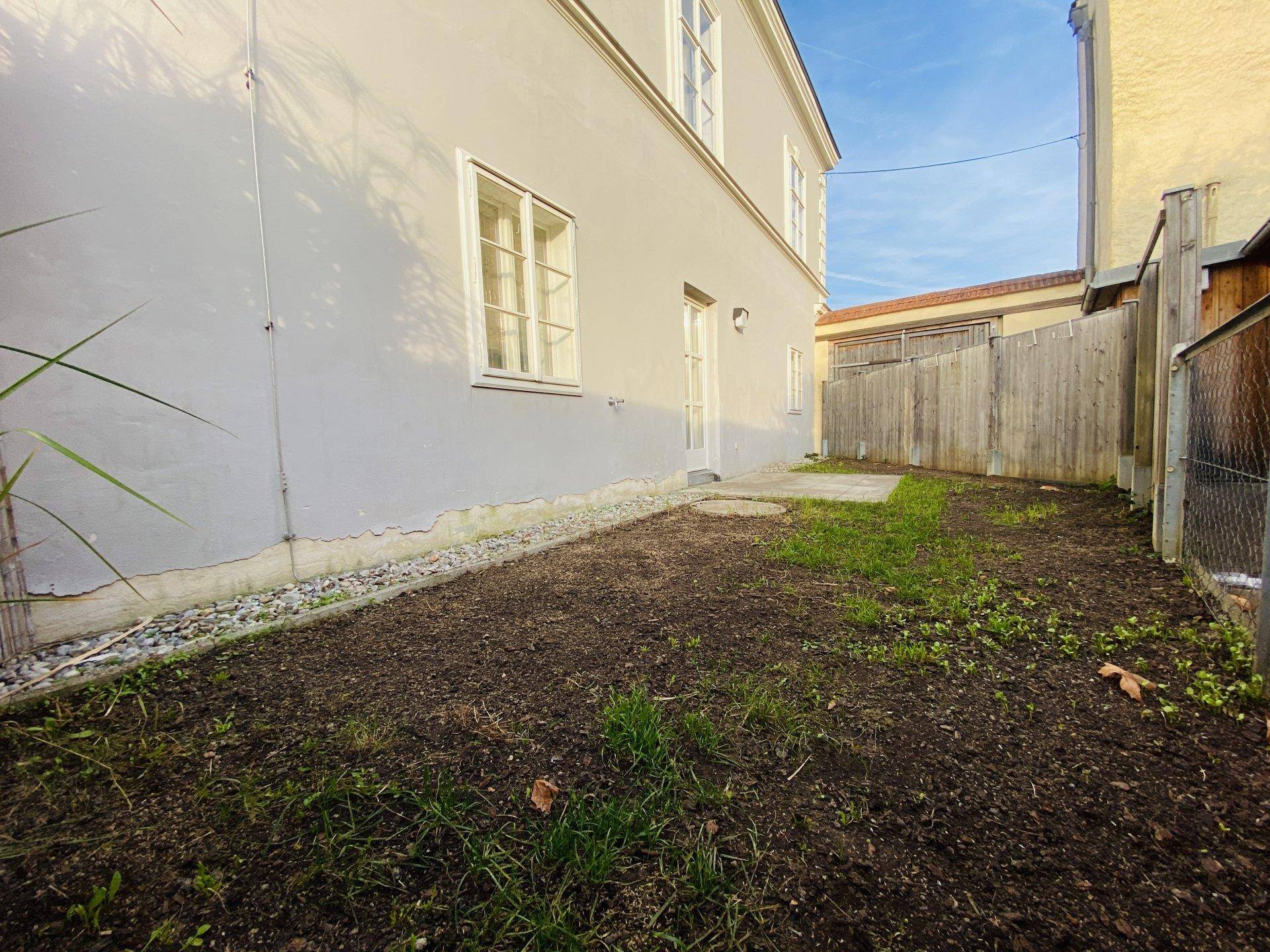 Kleiner Gartenbereich neben dem Gebäude mit frisch umgegrabener Erde und Holzzaun.