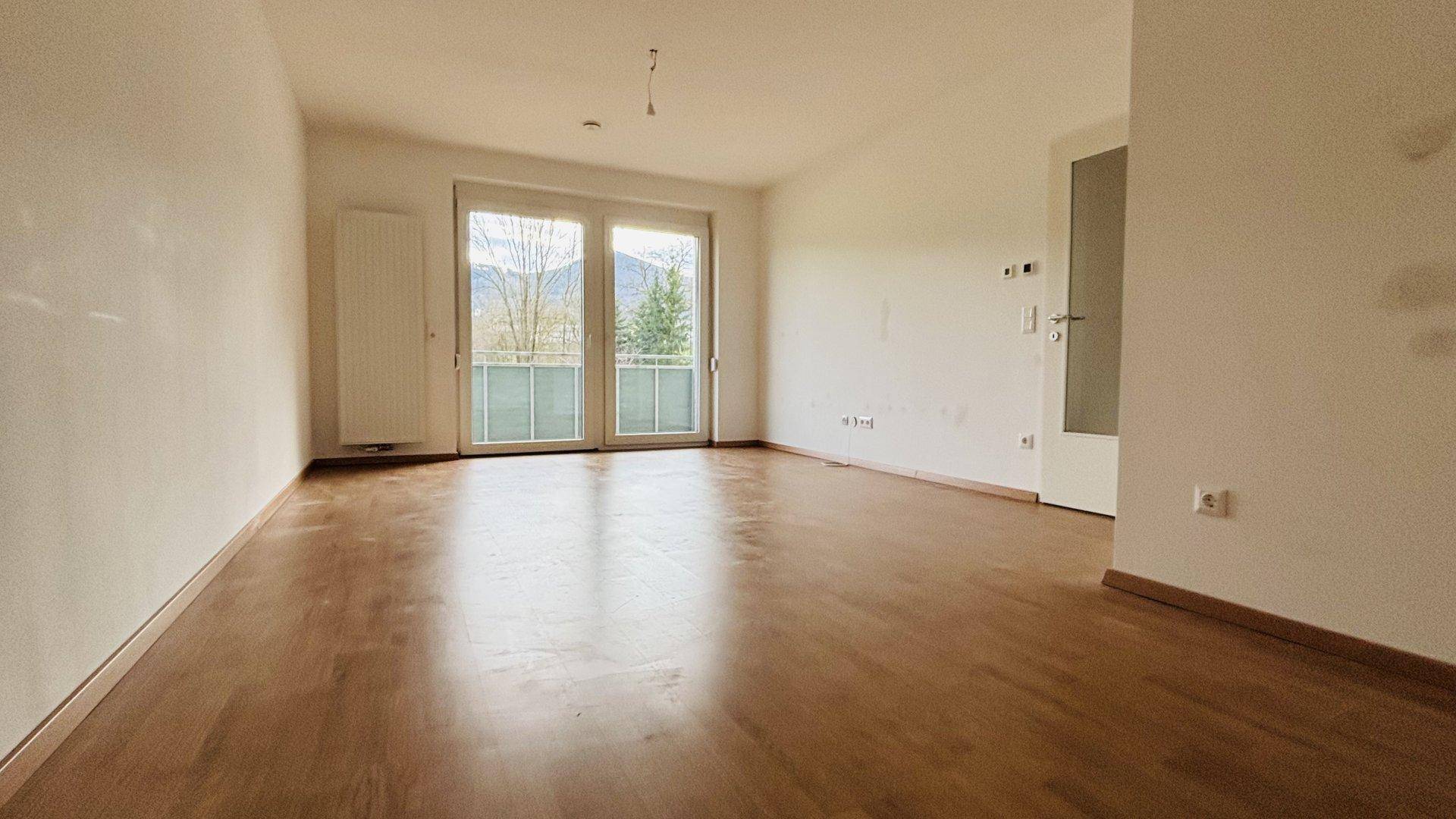 Heller Wohnbereich mit Holzboden und Balkonzugang, ideal für entspannte Momente.