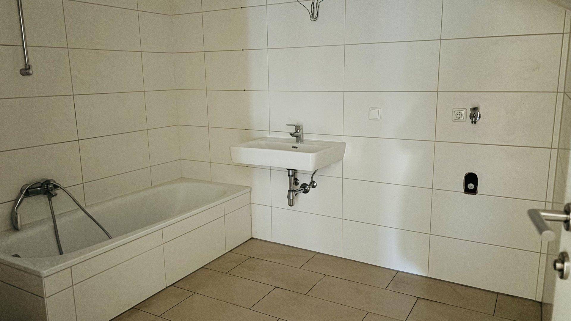 Funktionales Badezimmer mit weißen Fliesen, Badewanne und Waschbecken, bereit zur Nutzung.