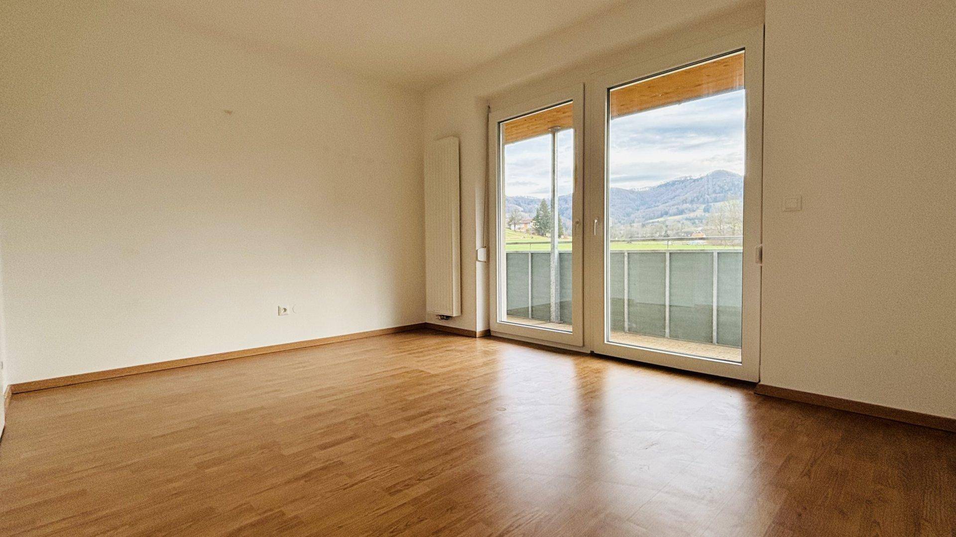 Geräumiges Zimmer mit Parkettboden und großen Fenstern, die viel Tageslicht hereinlassen.