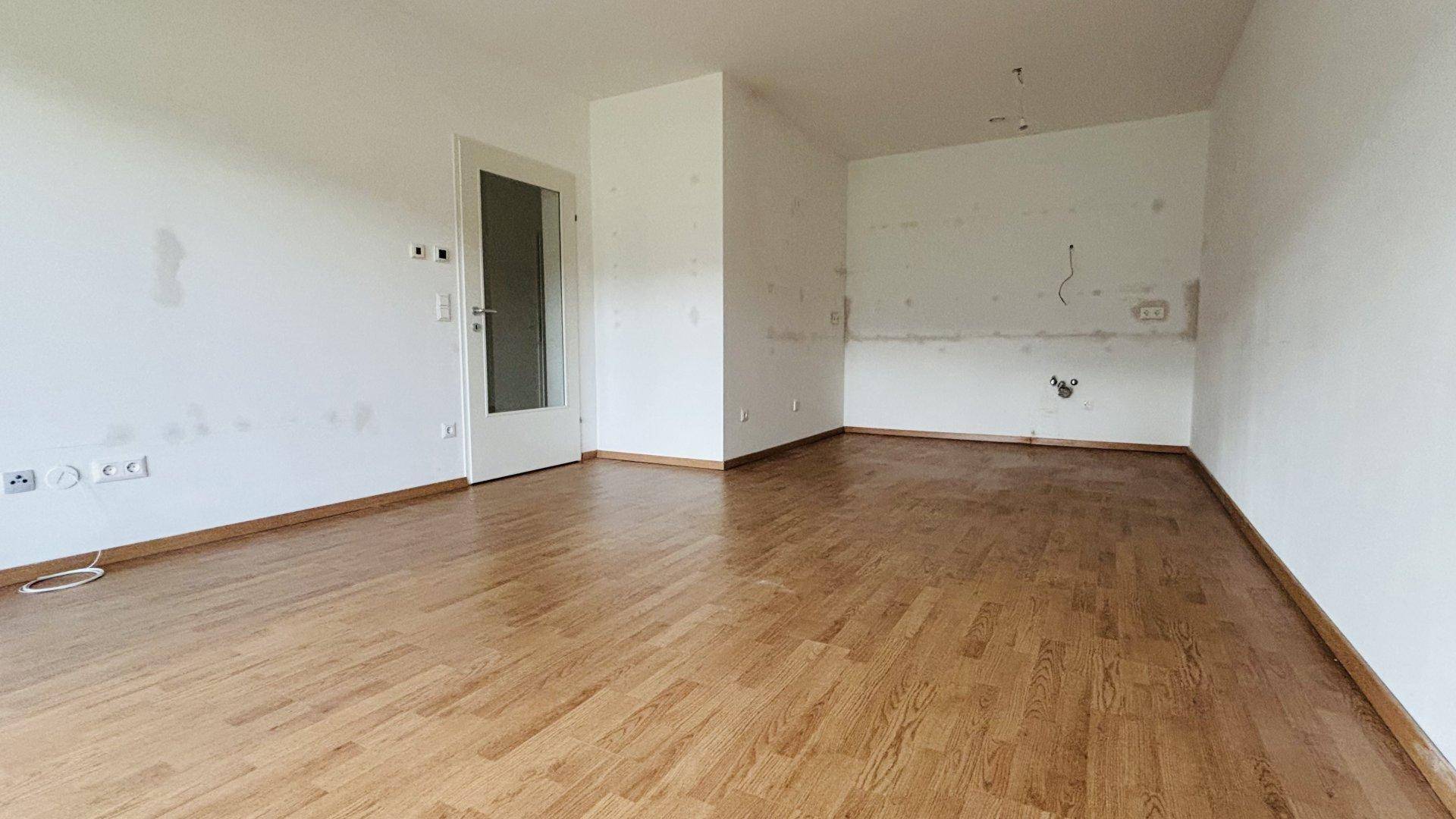 Geräumiger, unmöblierter Raum mit Parkettboden und Zugang zu weiteren Bereichen.