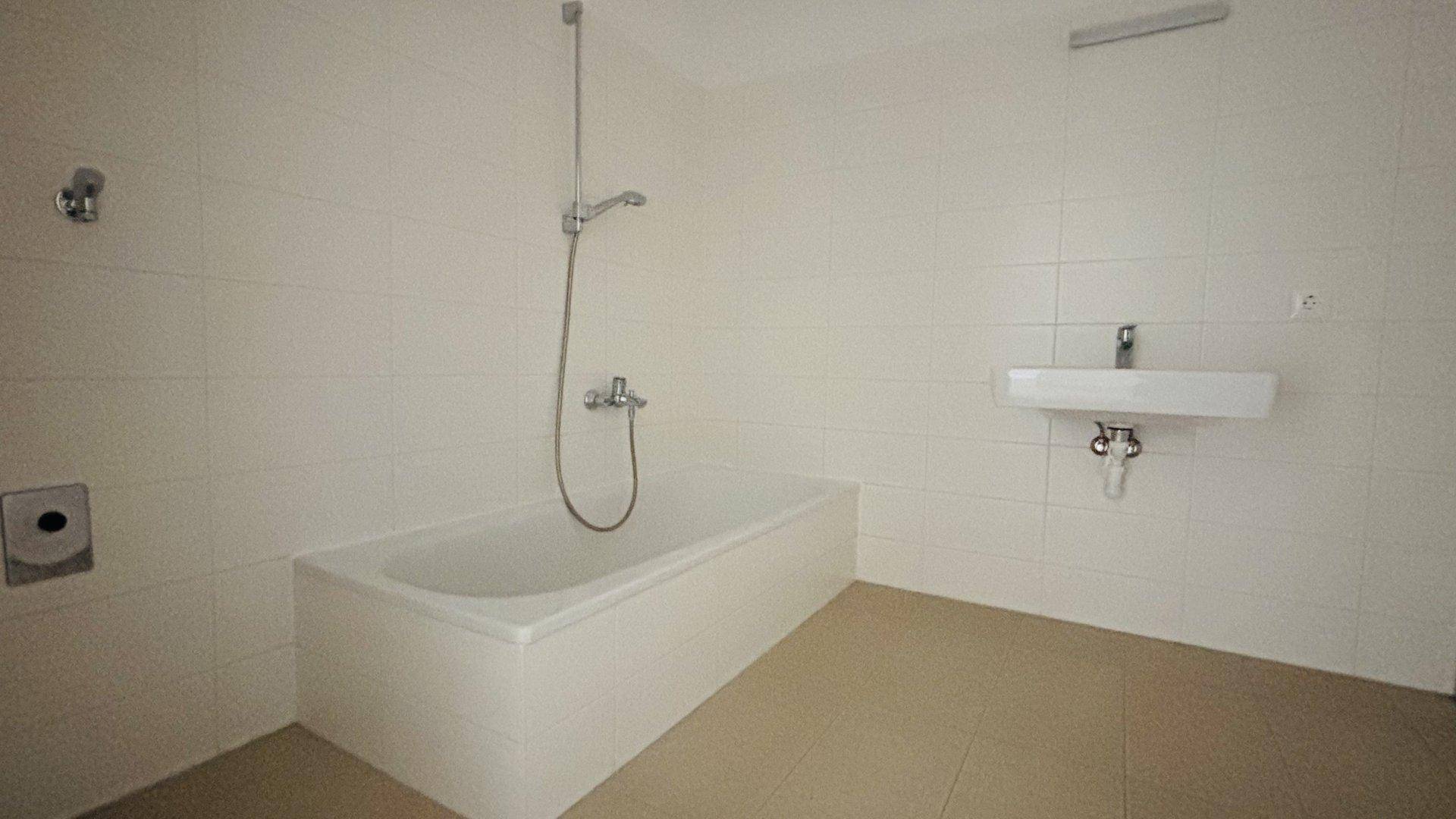 Helles Badezimmer mit Badewanne, Waschbecken und weißen Fliesen an den Wänden.