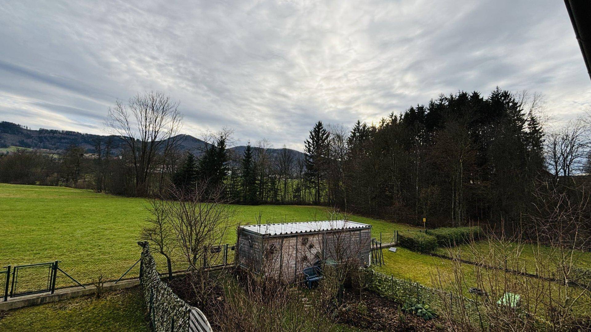 Panoramablick auf die ländliche Umgebung mit Feldern, Wäldern und Bergen im Hintergrund.