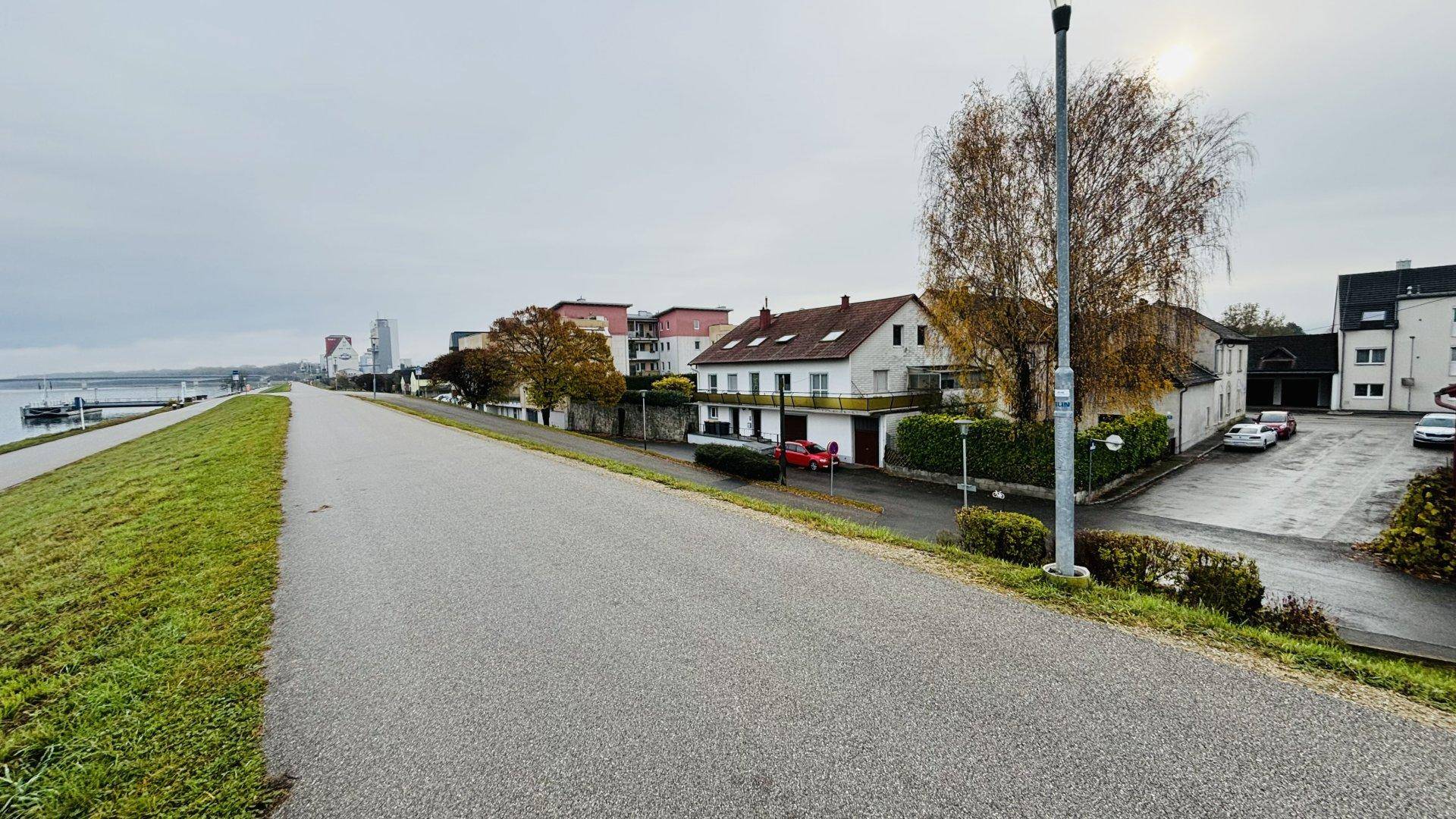 Uferpromenade entlang eines Gewässers mit Gebäuden und Bäumen im Herbstlaub.