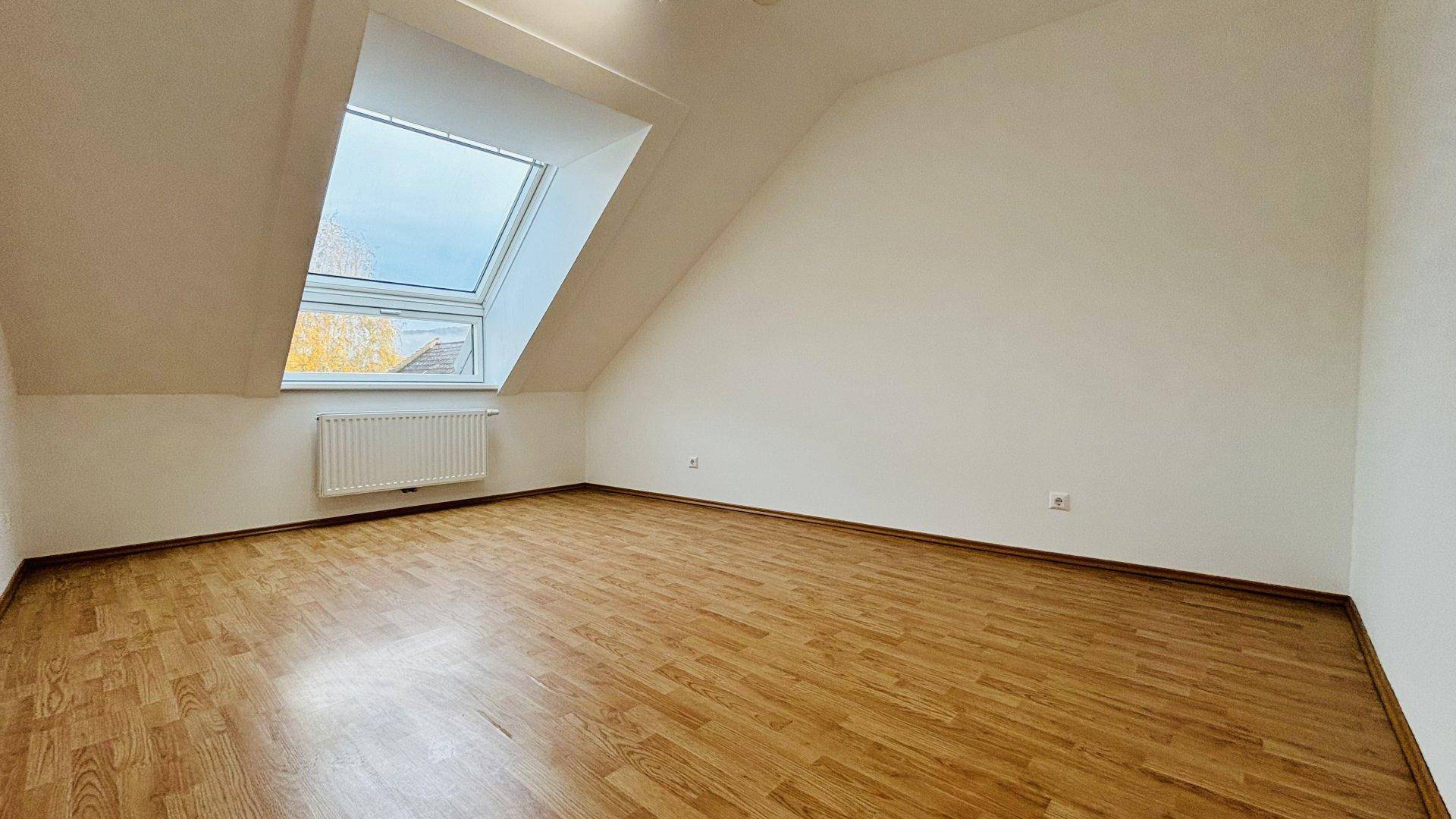 Geräumiges Dachzimmer mit Laminatboden, großem Dachfenster und weiß gestrichenen Wänden.