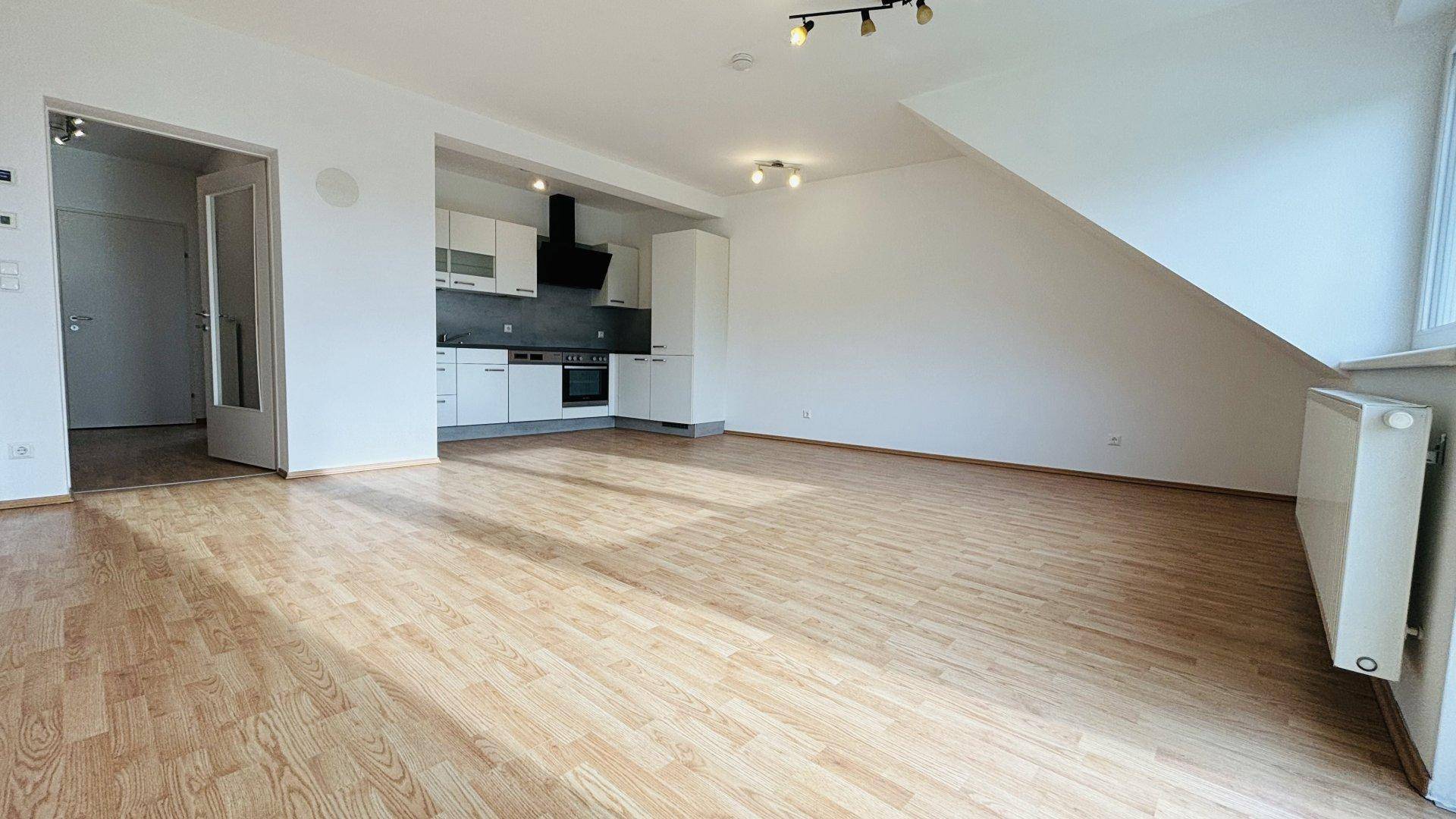 Heller Wohnbereich mit integrierter Küche, Laminatboden und Zugang zum Balkon.