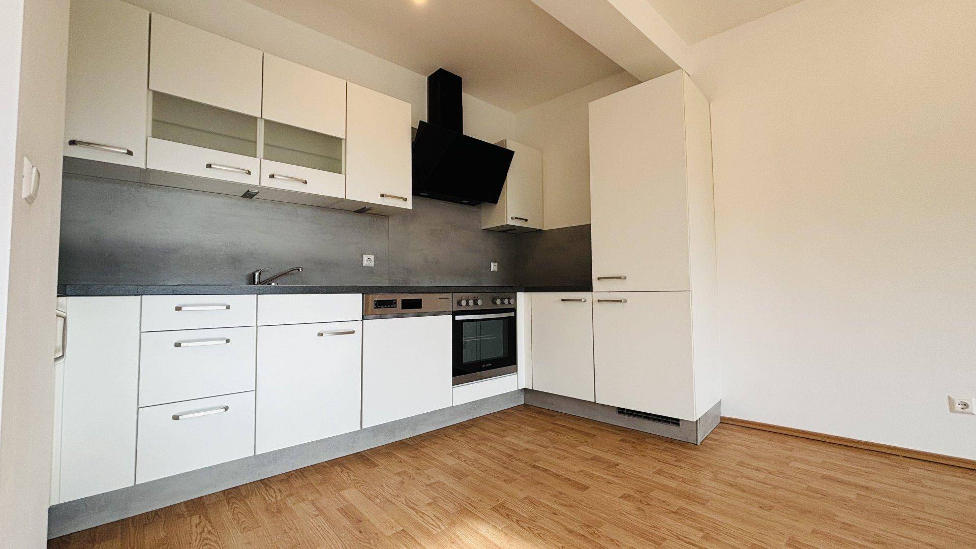 Moderne Einbauküche mit weißen Schränken, dunkler Arbeitsplatte und integrierten Geräten.