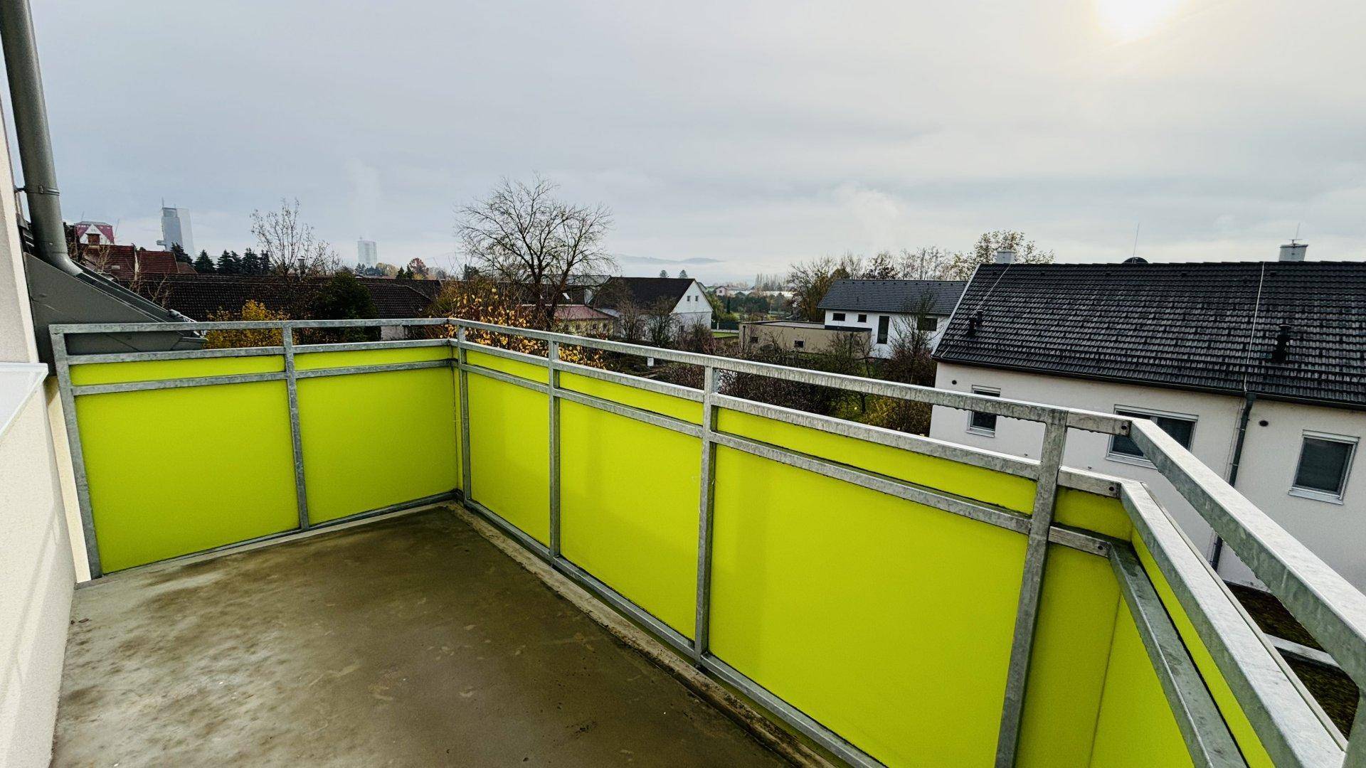 Geräumiger Balkon mit grünen Brüstungen und Blick auf die umliegenden Häuser und Landschaft.