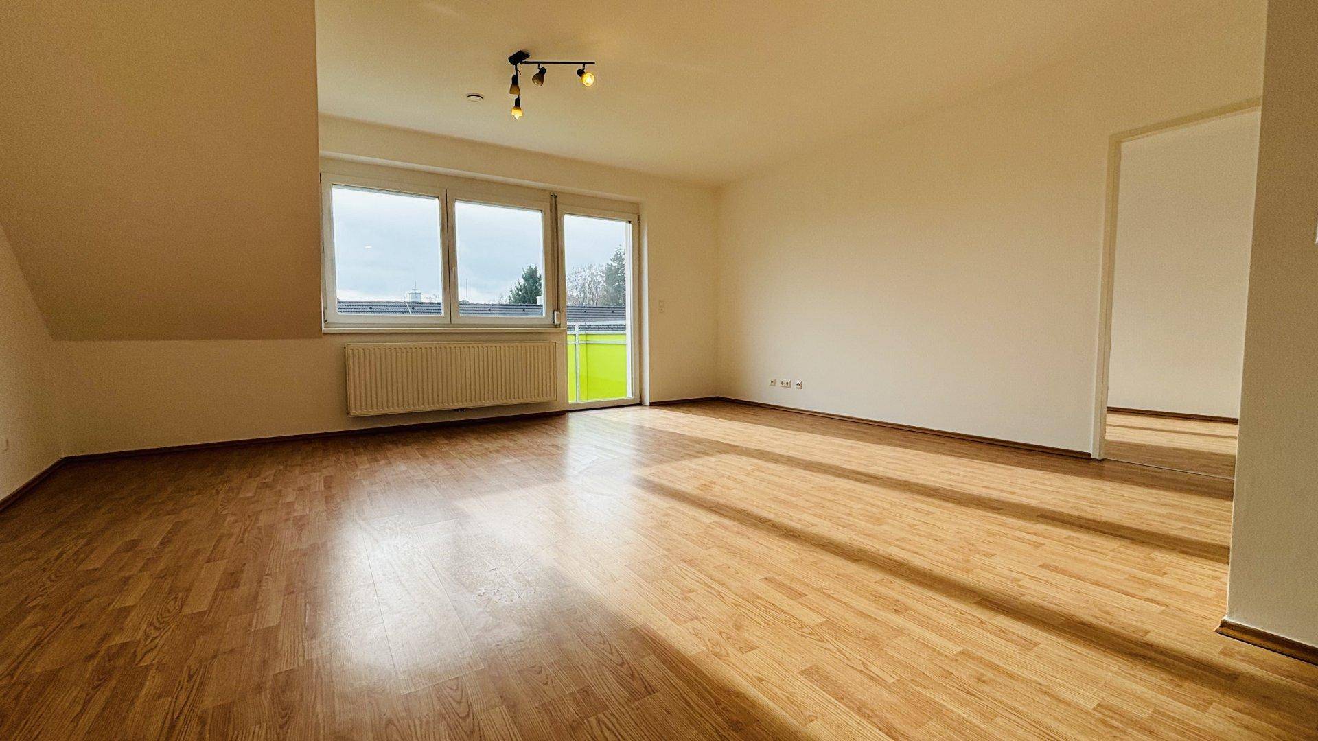 Heller Wohnbereich mit Laminatboden und großem Fenster mit Zugang zum Balkon.