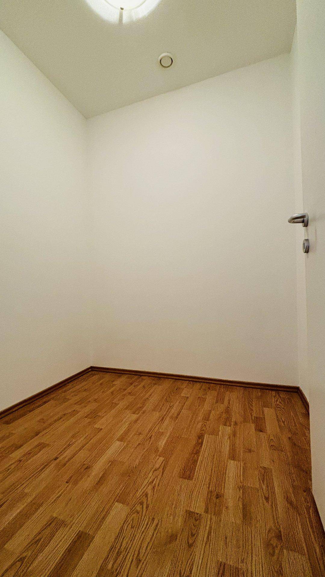Kleiner, leerer Raum mit Laminatboden und weiß gestrichenen Wänden.