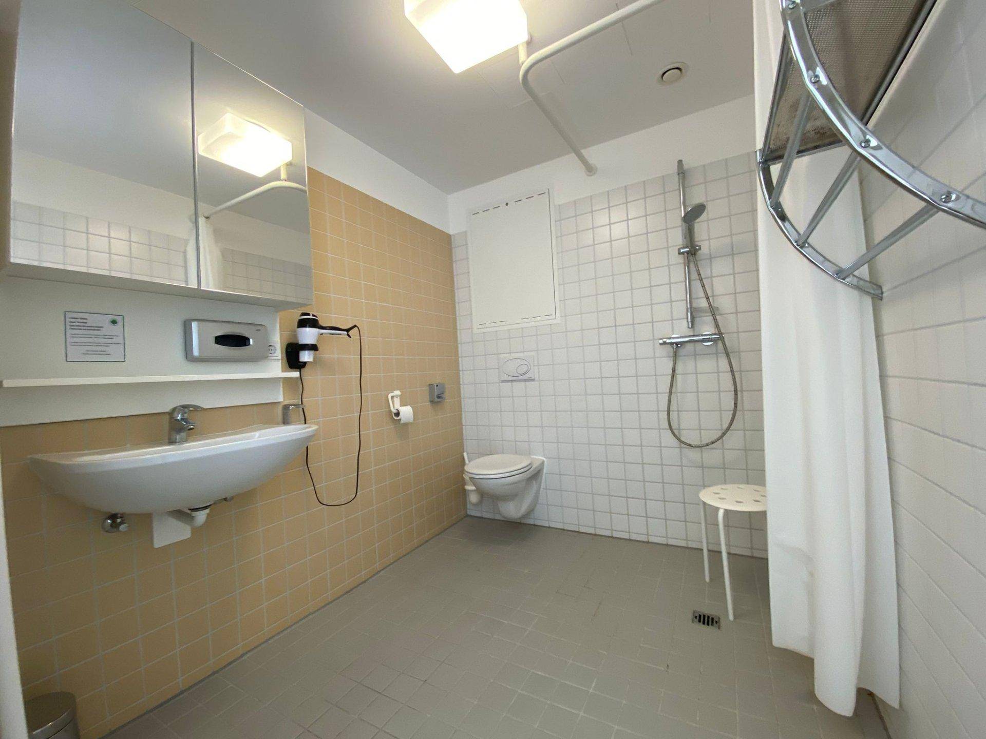 Funktionales Badezimmer mit Dusche, WC, Waschbecken und Spiegelschrank, gefliest in Beige und Weiß.