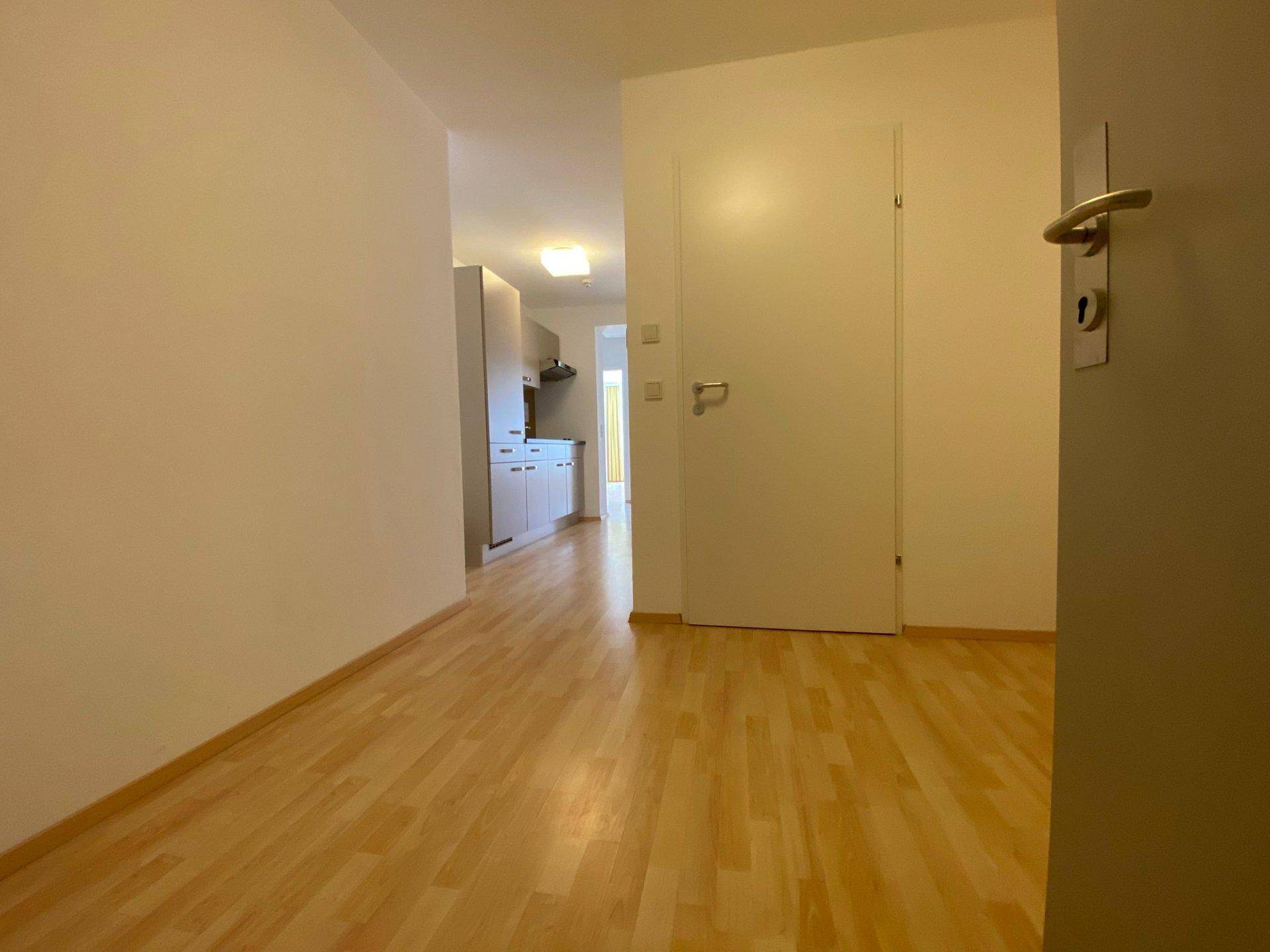 Heller Flur mit hellem Laminatboden, der zu einer Küchenzeile und weiteren Räumen führt.