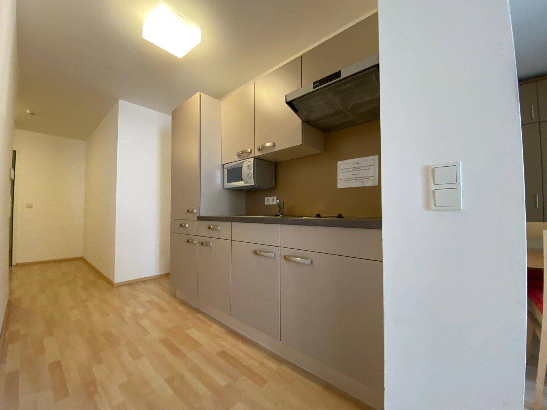 Kompakte Küchenzeile mit Mikrowelle und Dunstabzugshaube, ideal für kleine Wohnbereiche.