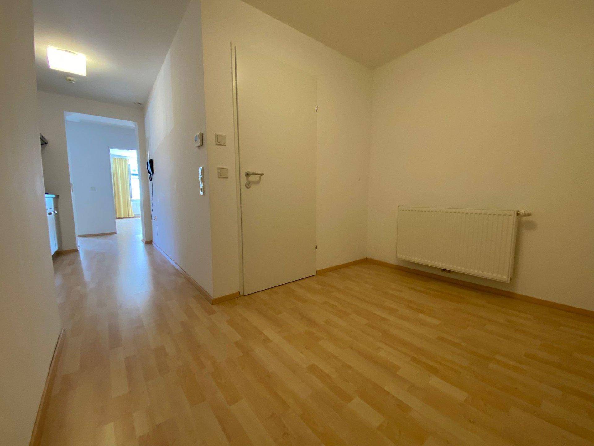 Geräumiger Flur mit Laminatboden und Heizkörper, der den Zugang zu verschiedenen Zimmern ermöglicht.
