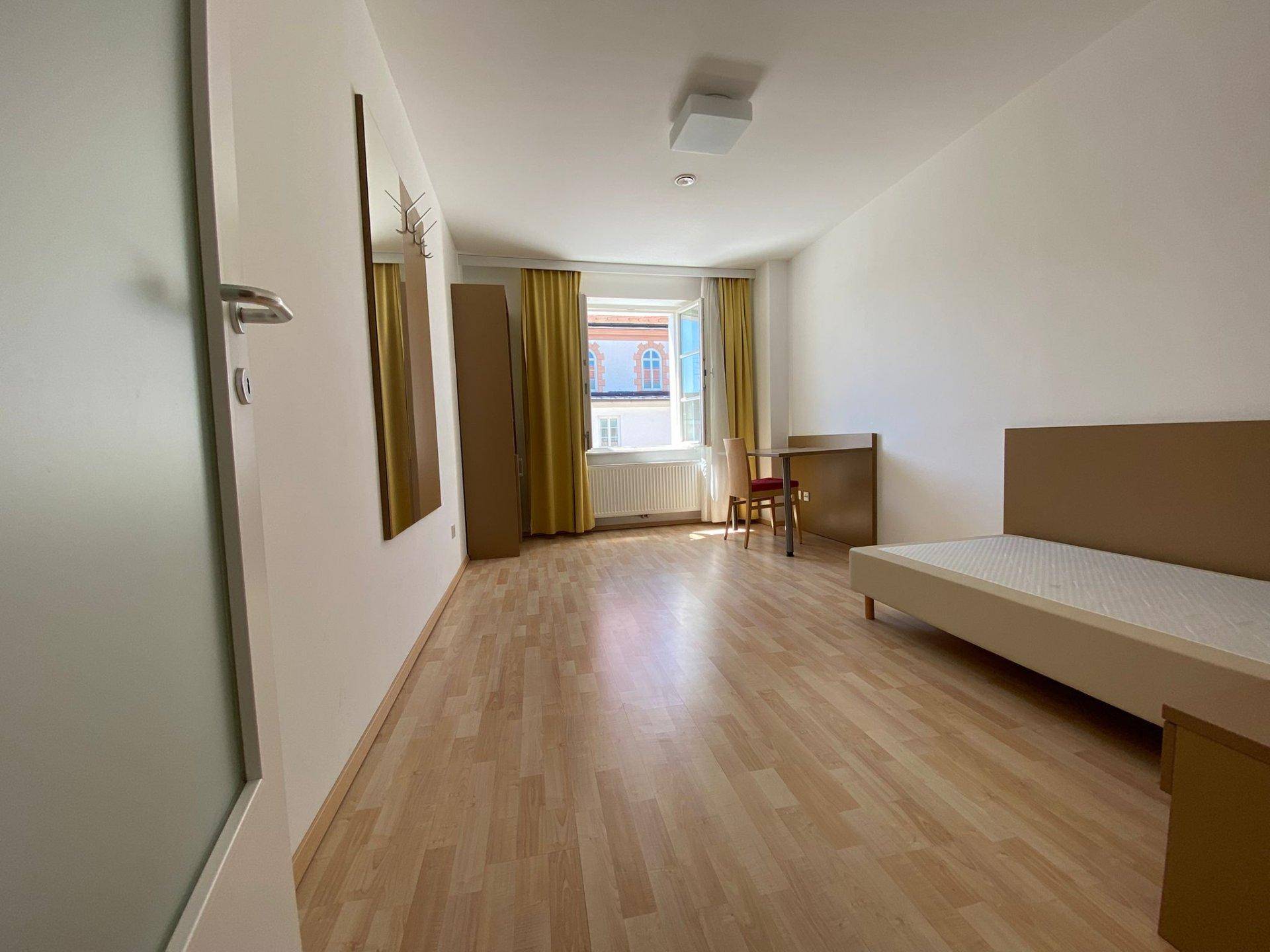 Geräumiges Schlafzimmer mit Einzelbett, Spiegel und Schrank, ausgestattet mit Laminatboden.