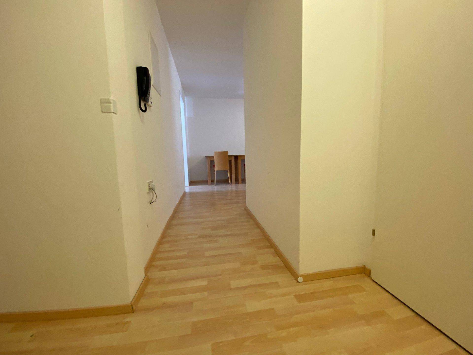 Langer, heller Flur mit Laminatboden, der zu einem weiteren Raum führt.