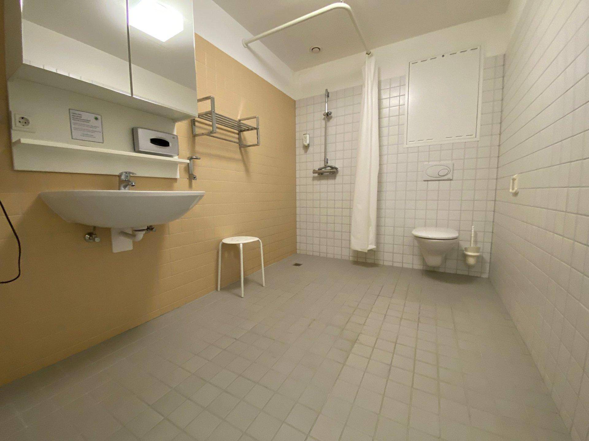 Funktionales Badezimmer mit beigen und weißen Fliesen, Dusche und WC.