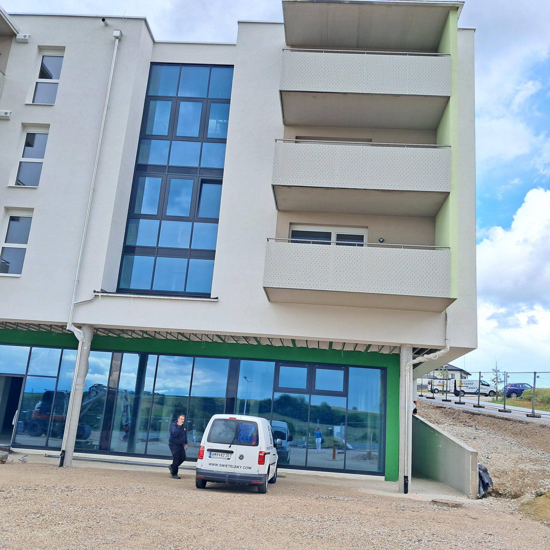 Moderne Gebäudeecke mit großen Fensterfronten und Balkonen, teilweise noch im Bau.