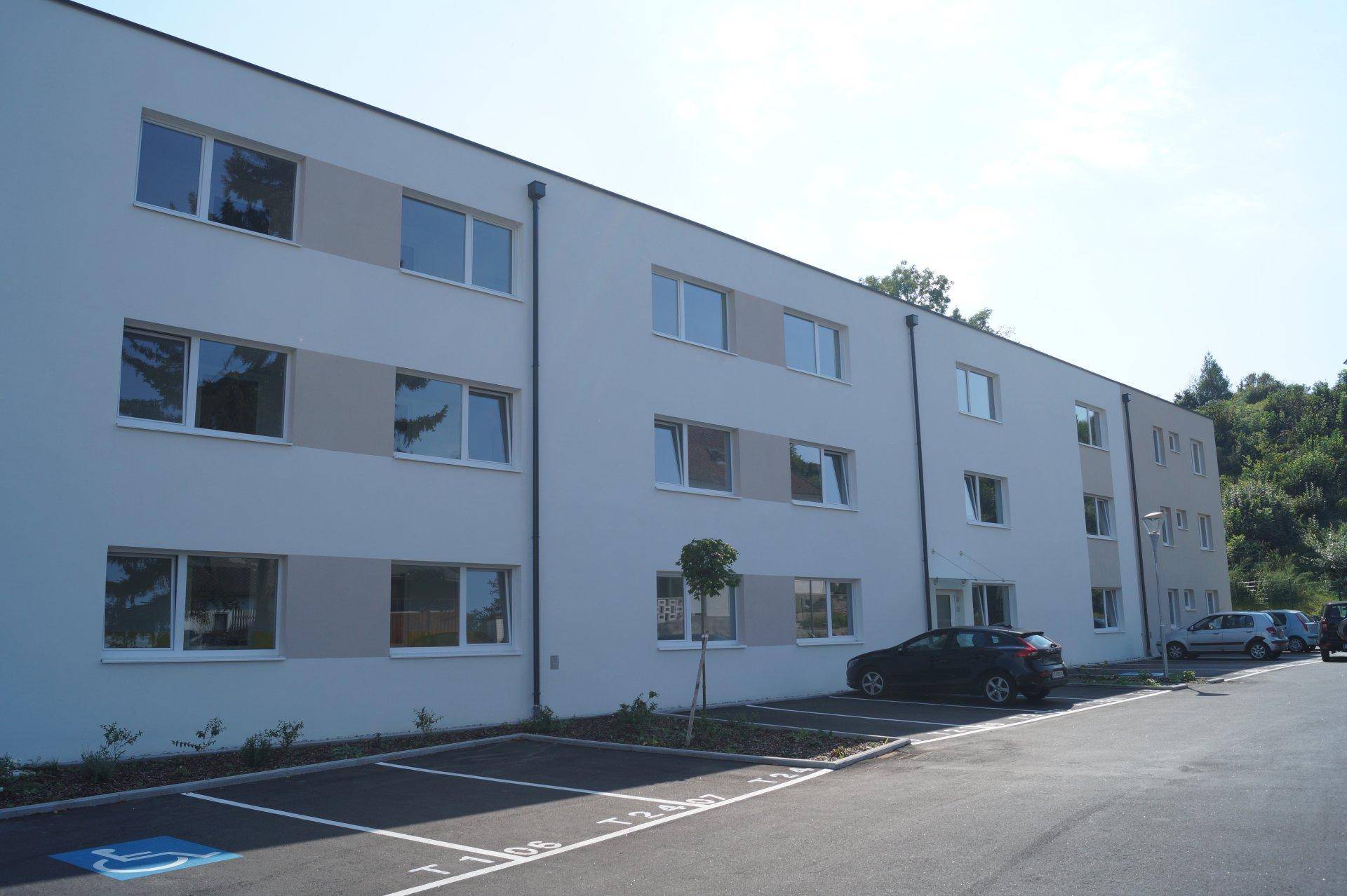 Moderne Apartmentgebäude mit Parkplätzen, inklusive eines barrierefreien Stellplatzes, vor der Fassade.
