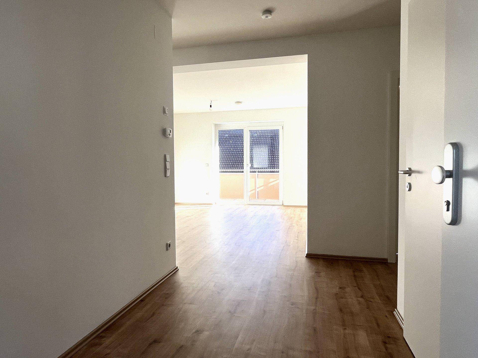 Heller Flur mit Holzboden, der zu einem lichtdurchfluteten Wohnbereich mit Balkonzugang führt.