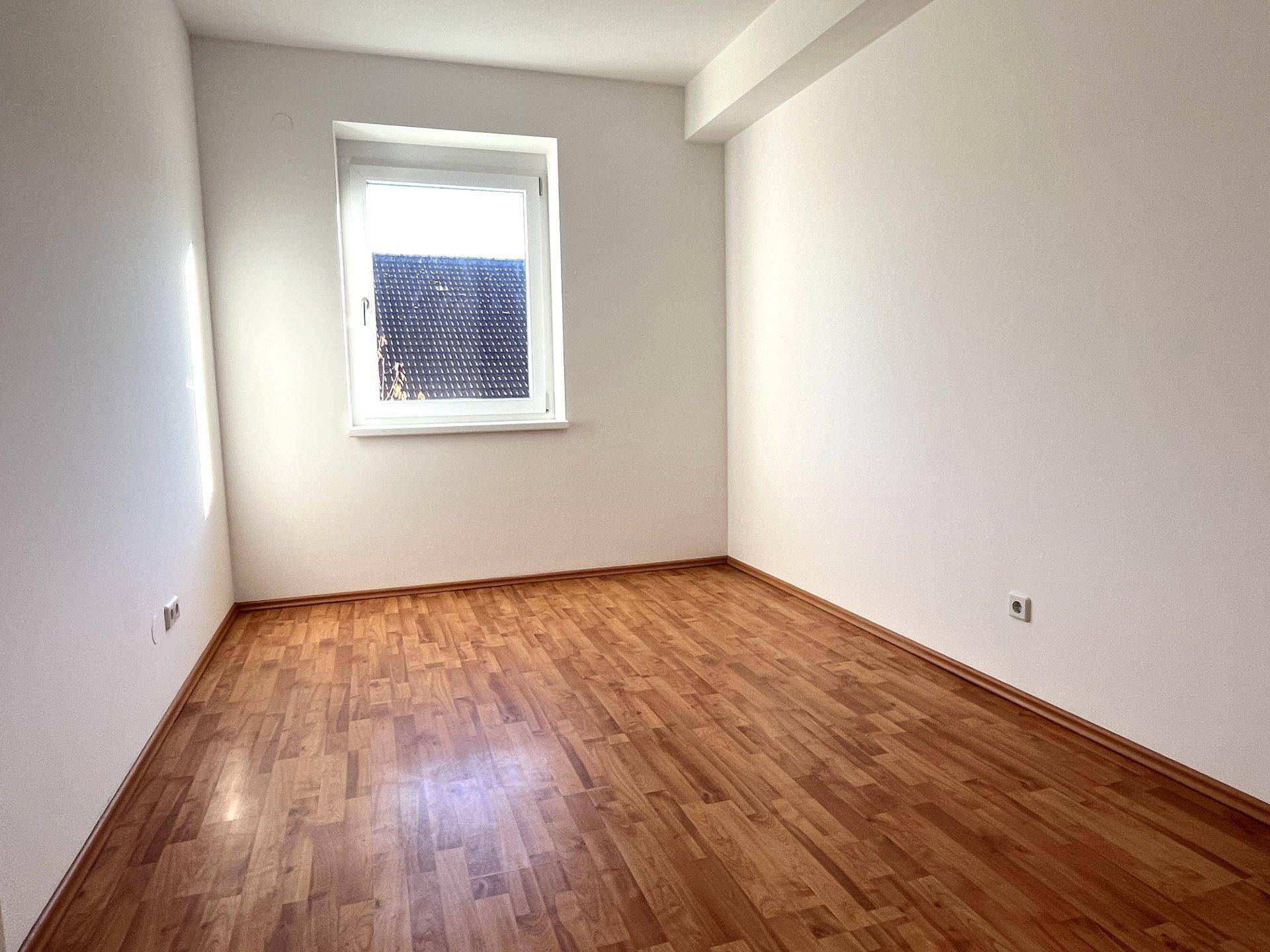 Ruhiges Schlafzimmer mit Holzboden und einem Fenster, das eine angenehme Atmosphäre schafft.