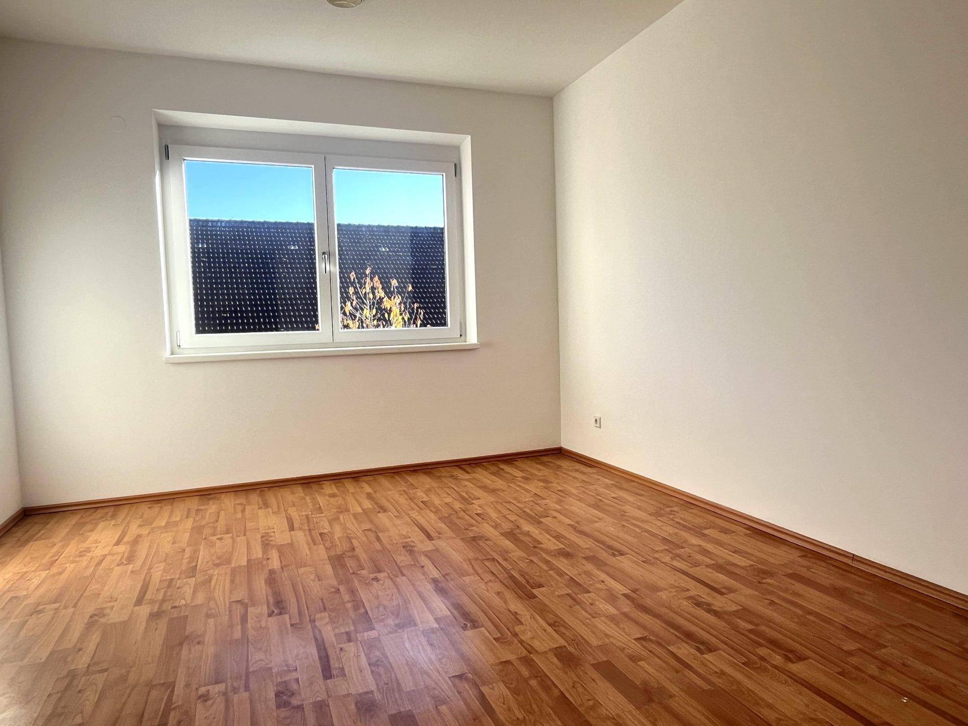 Helles Schlafzimmer mit Holzboden und einem großen Fenster, das viel Tageslicht hereinlässt.