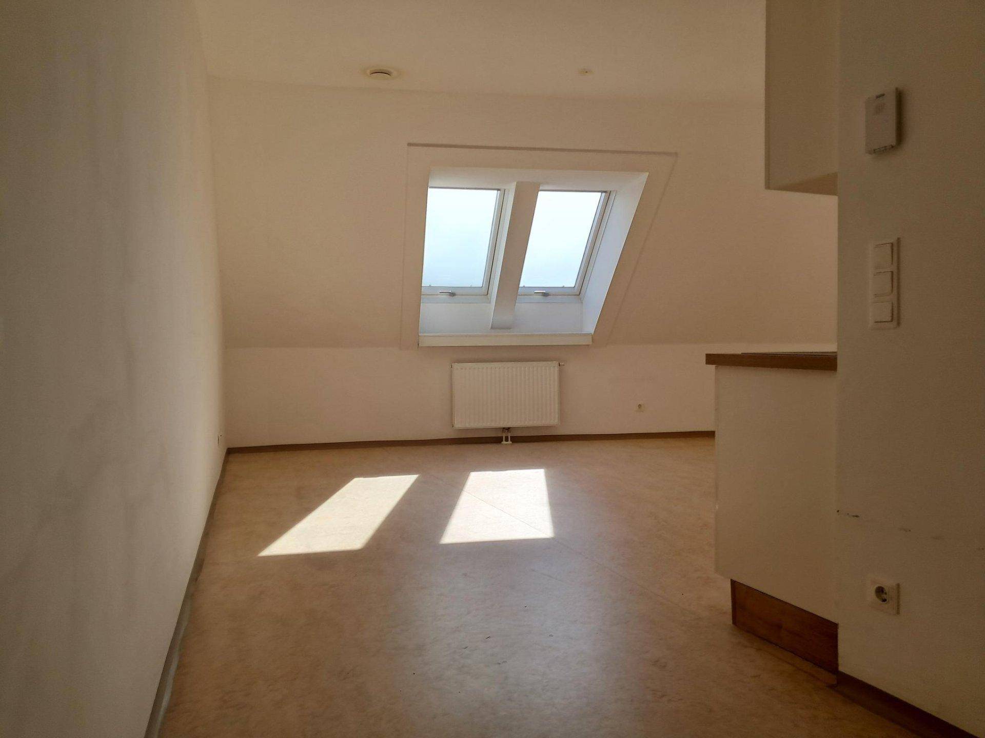 Heller Wohnraum im Dachgeschoss mit schrägen Wänden, Dachfenstern und hellem Laminatboden.
