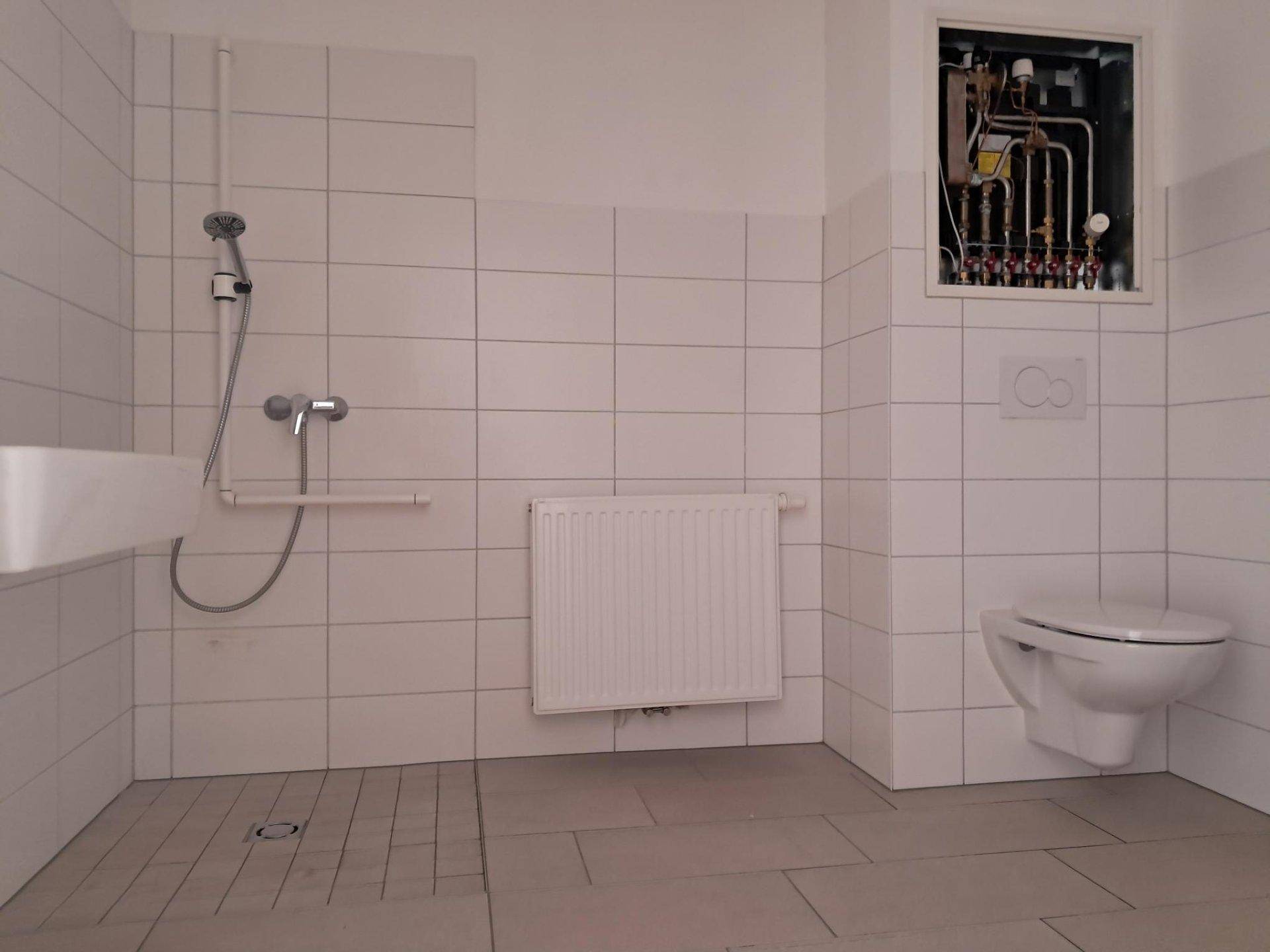 Modernes Badezimmer mit weißen Fliesen, ebenerdiger Dusche und wandhängendem WC.