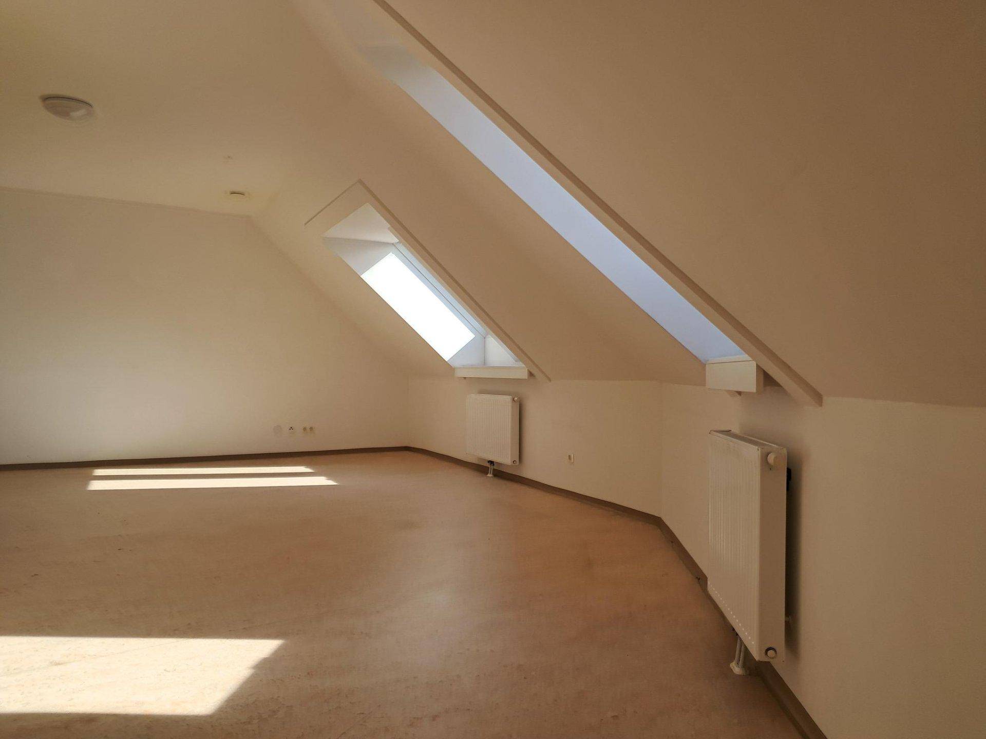 Geräumiger Wohnraum im Dachgeschoss mit schrägen Wänden, Dachfenstern und hellem Bodenbelag.